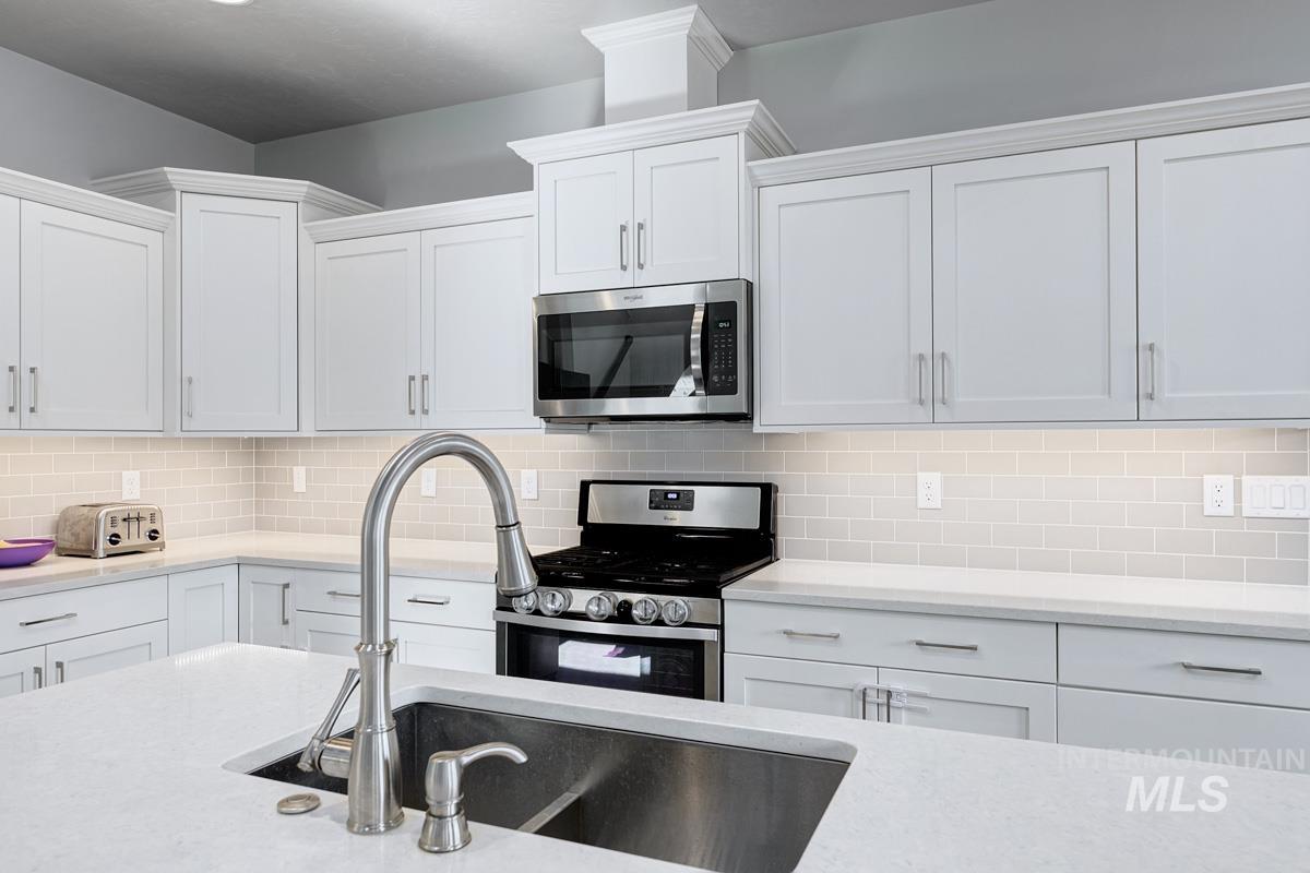 Kitchen featuring stainless steel appliances, white cabinetry, tasteful backsplash, and light stone counters