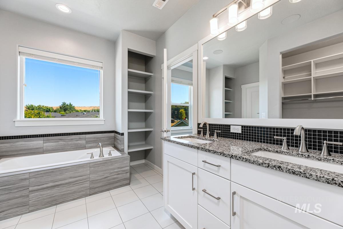 Bathroom featuring double vanity, tile patterned floors, tiled tub, a spacious closet, and recessed lighting