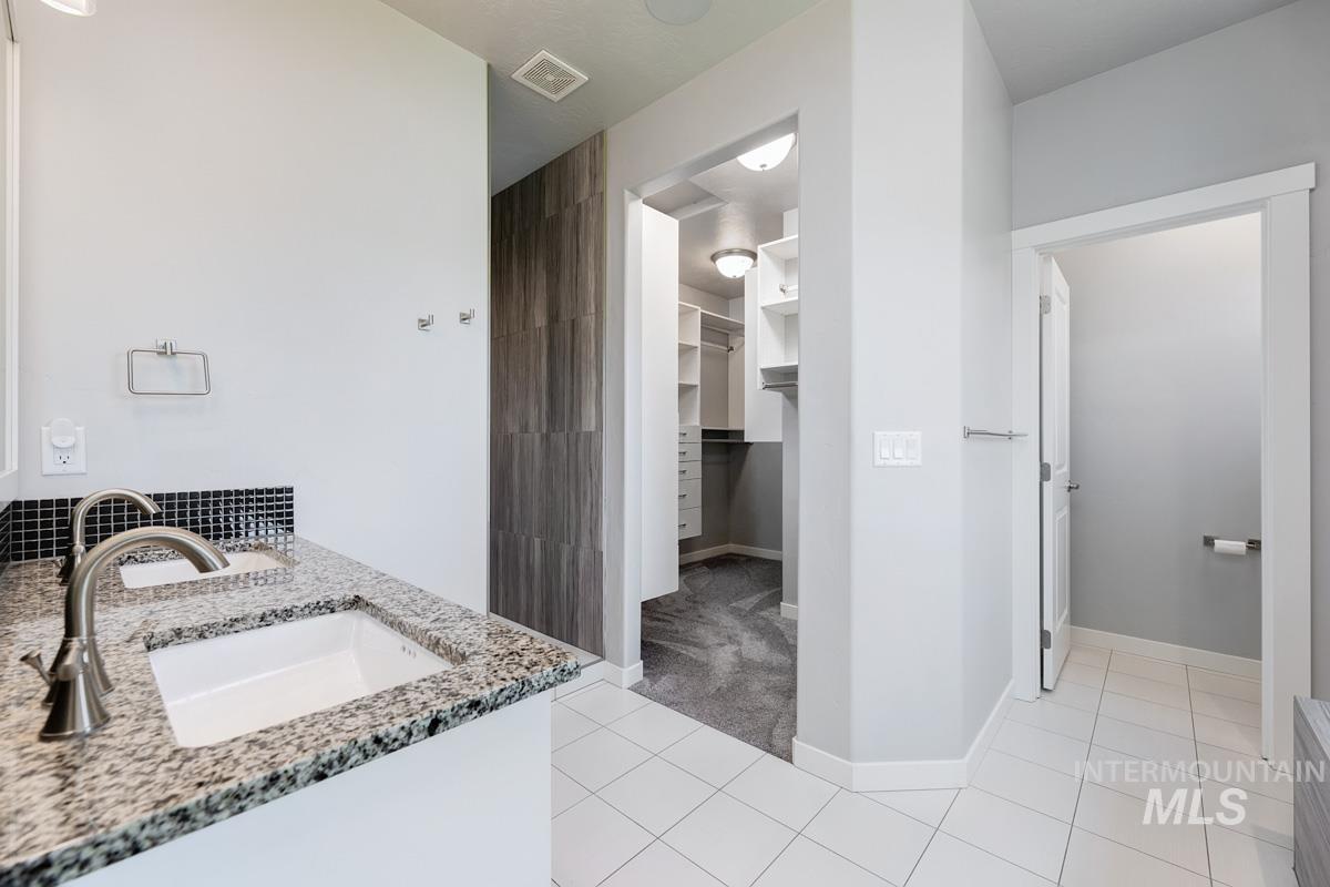 Full bath with double vanity, tile patterned flooring, and a spacious closet