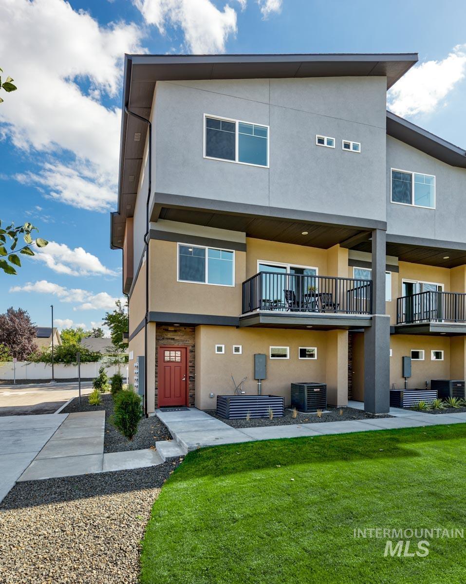 Rear view of house featuring stucco siding, a balcony, and a yard