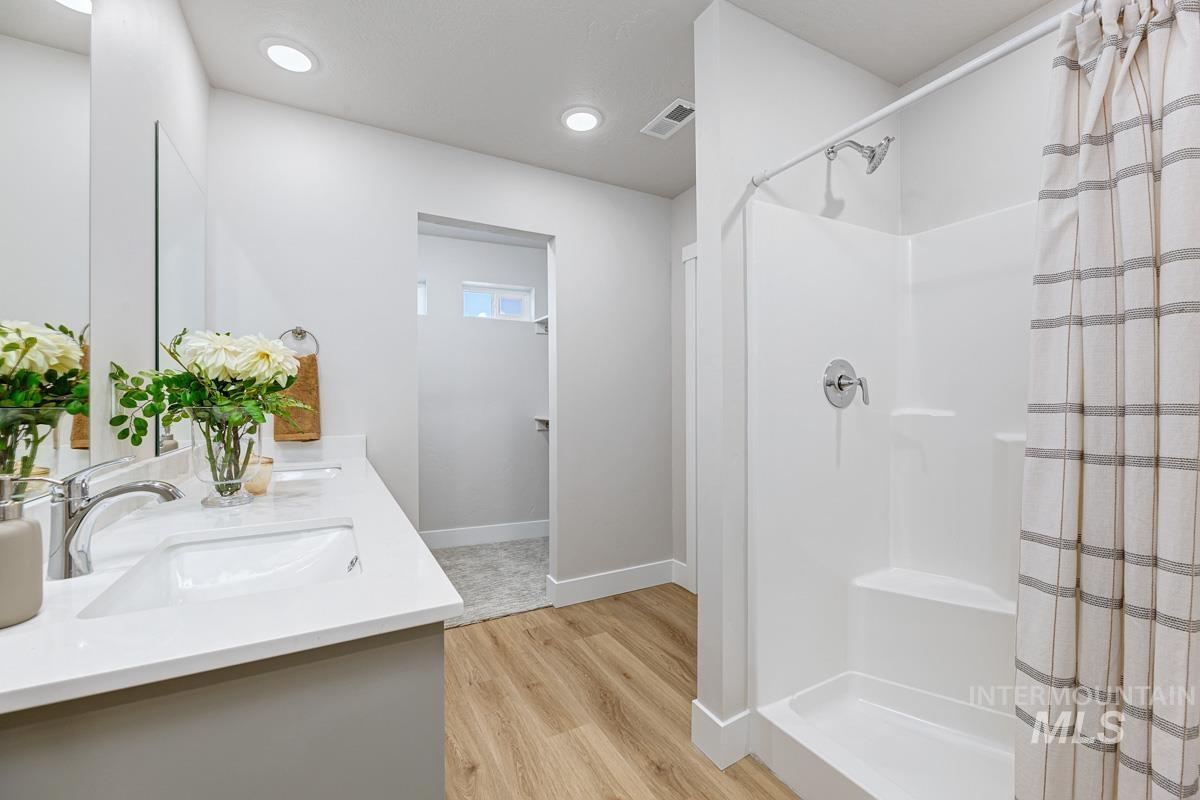 Full bathroom featuring a stall shower, double vanity, light wood-style flooring, and recessed lighting