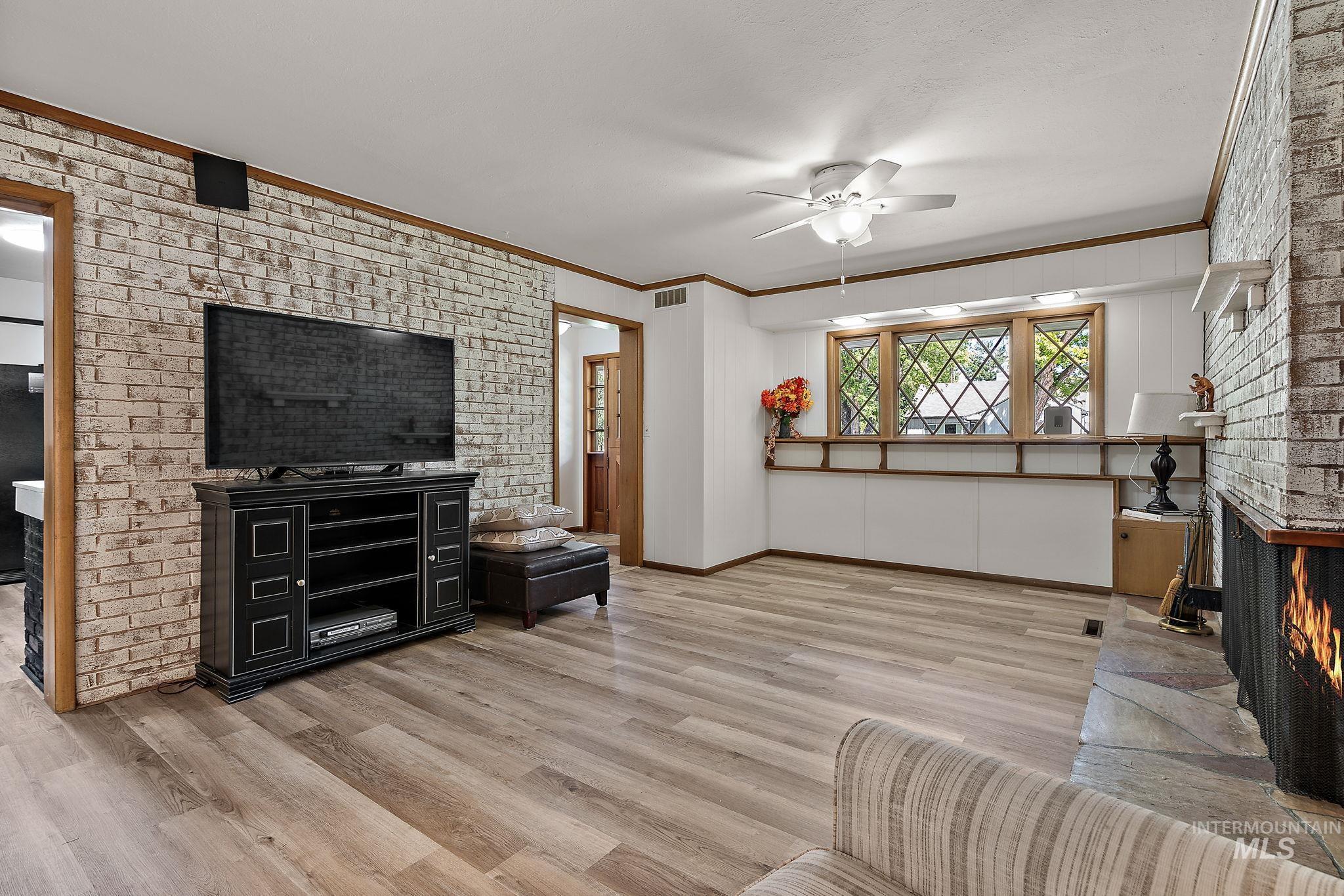 Living room featuring crown molding, brick wall, a fireplace, a ceiling fan, and wood finished floors