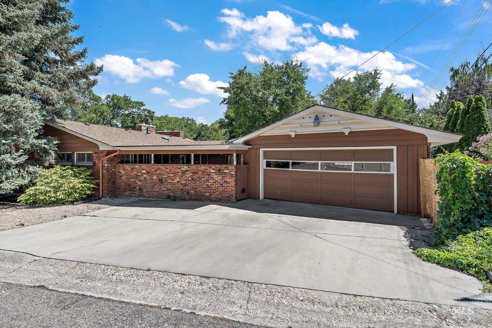 Ranch-style house featuring brick siding, an attached garage, a chimney, and driveway