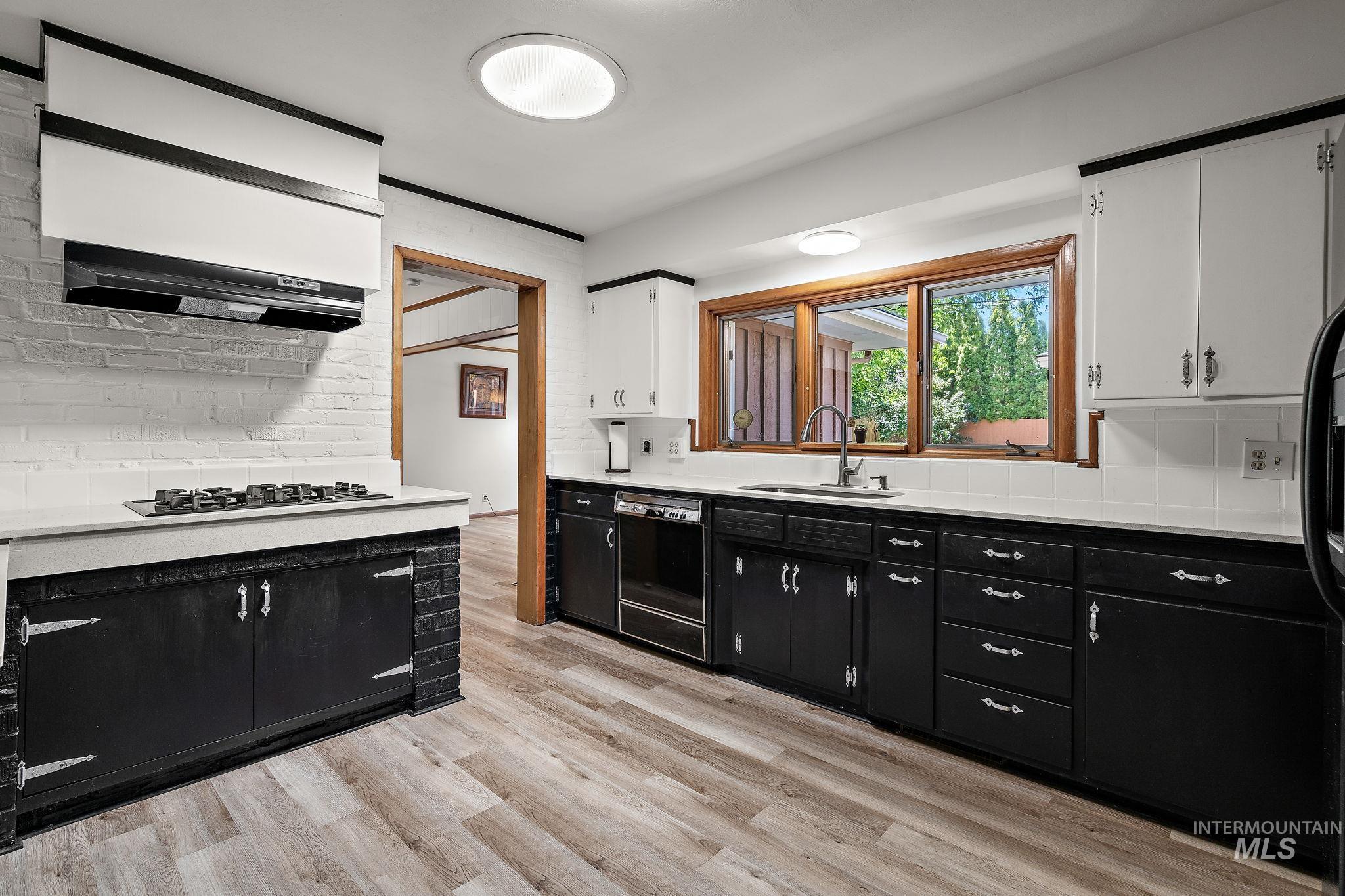 Kitchen featuring dark cabinets, tasteful backsplash, white cabinets, light wood-style floors, and black appliances