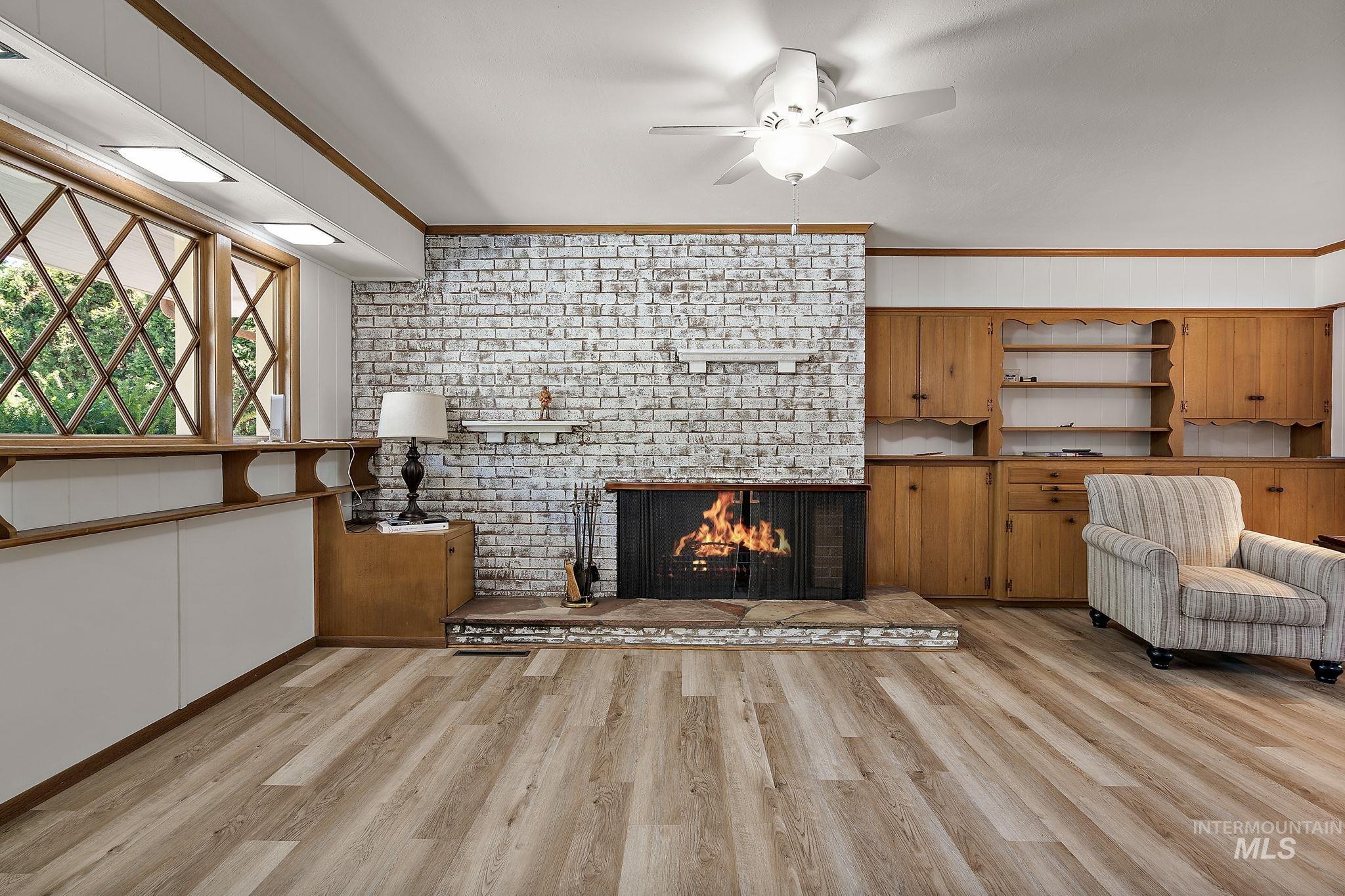 Unfurnished living room featuring crown molding, a brick fireplace, light wood finished floors, and ceiling fan