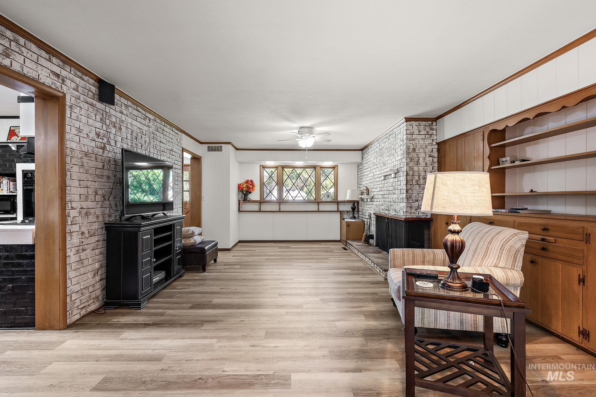 Living room featuring brick wall, ornamental molding, ceiling fan, light wood-type flooring, and built in shelves
