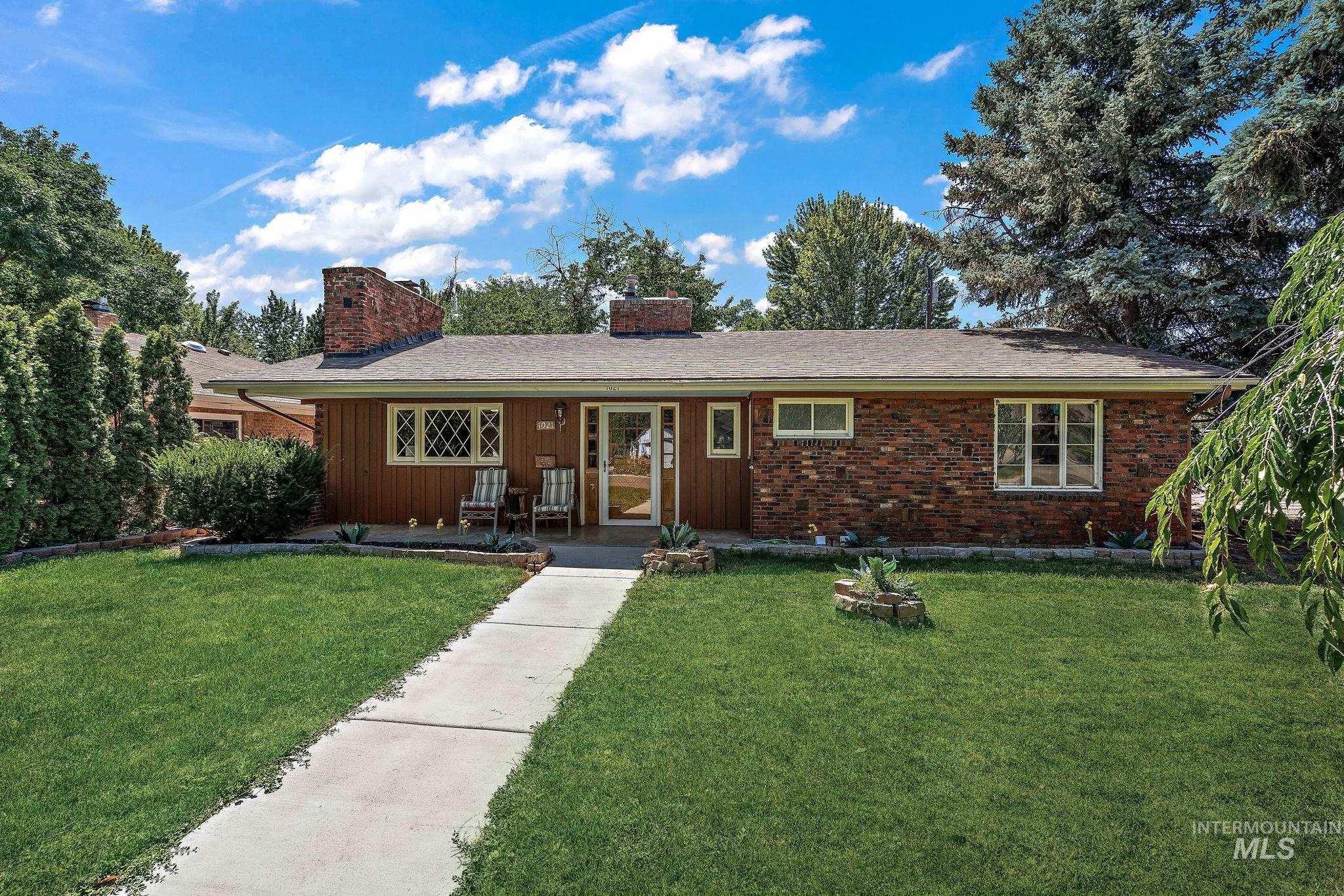 Ranch-style home featuring a chimney, a front lawn, board and batten siding, and brick siding