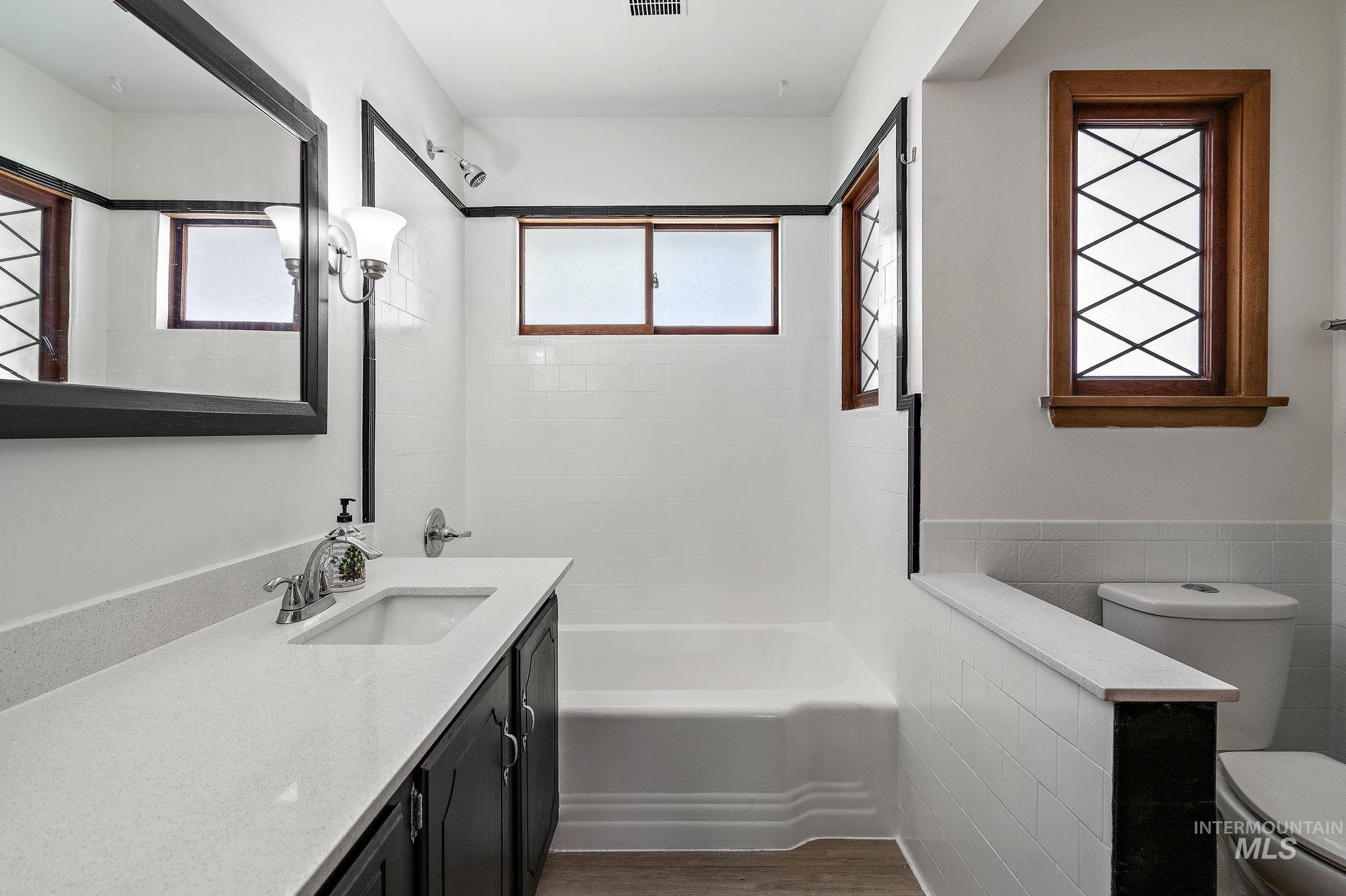 Bathroom with vanity, bathtub / shower combination, wood finished floors, tile walls, and a wainscoted wall