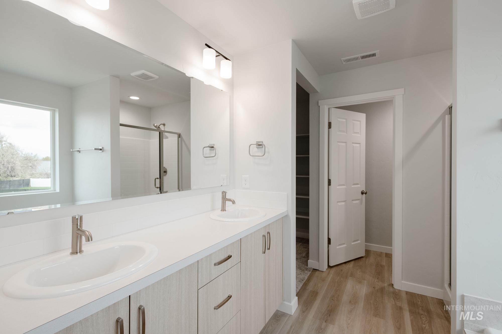 Bathroom featuring a shower stall, double vanity, light wood-type flooring, and a spacious closet