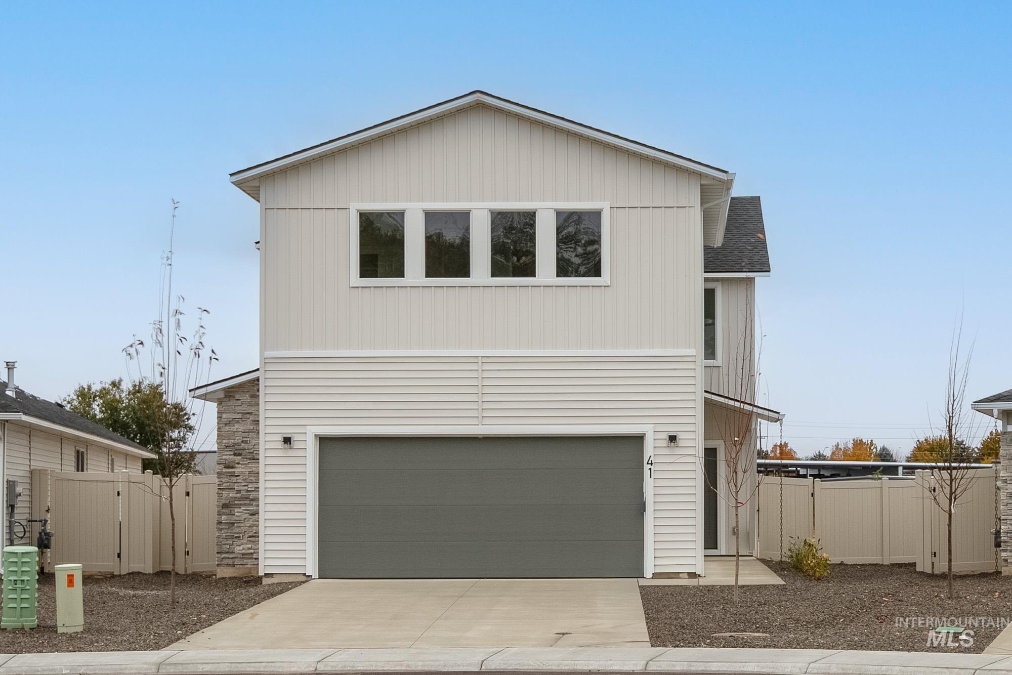 View of front facade featuring concrete driveway, a shingled roof, an attached garage, and stone siding