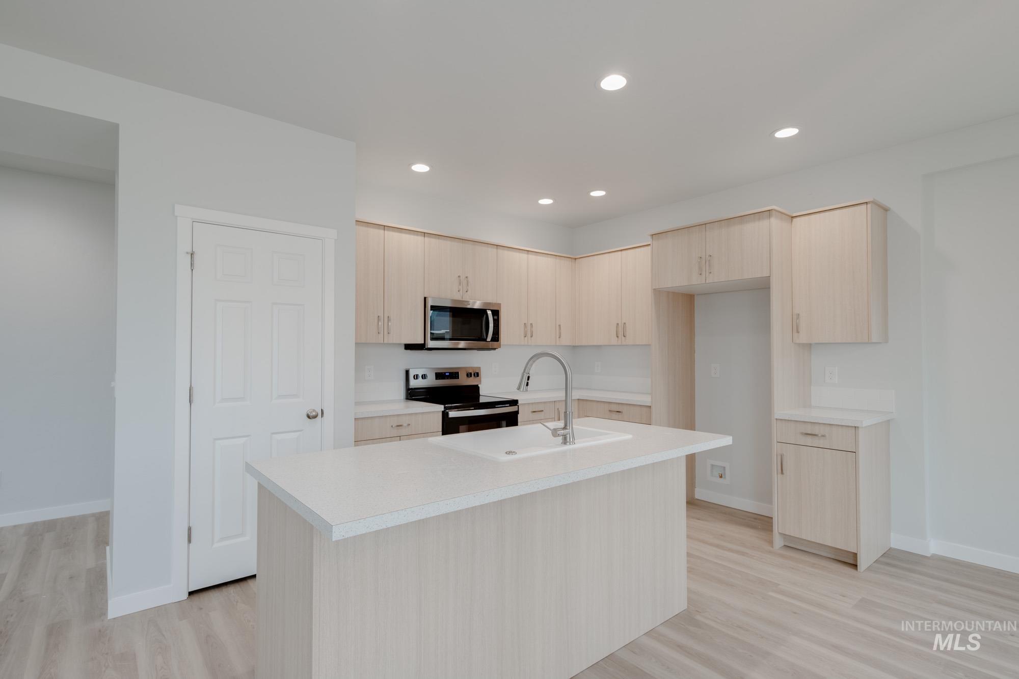 Kitchen with light brown cabinetry, light countertops, recessed lighting, light wood-style floors, and stainless steel appliances