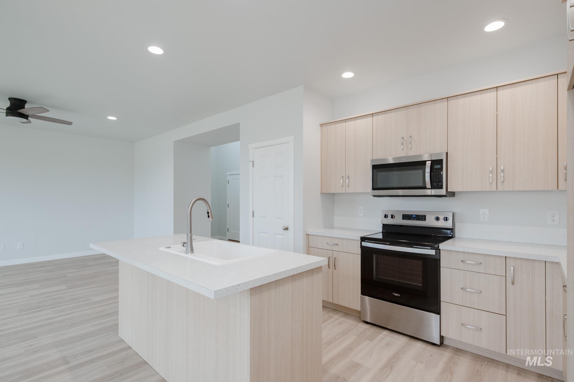 Kitchen with light brown cabinetry, stainless steel appliances, light countertops, recessed lighting, and light wood-type flooring