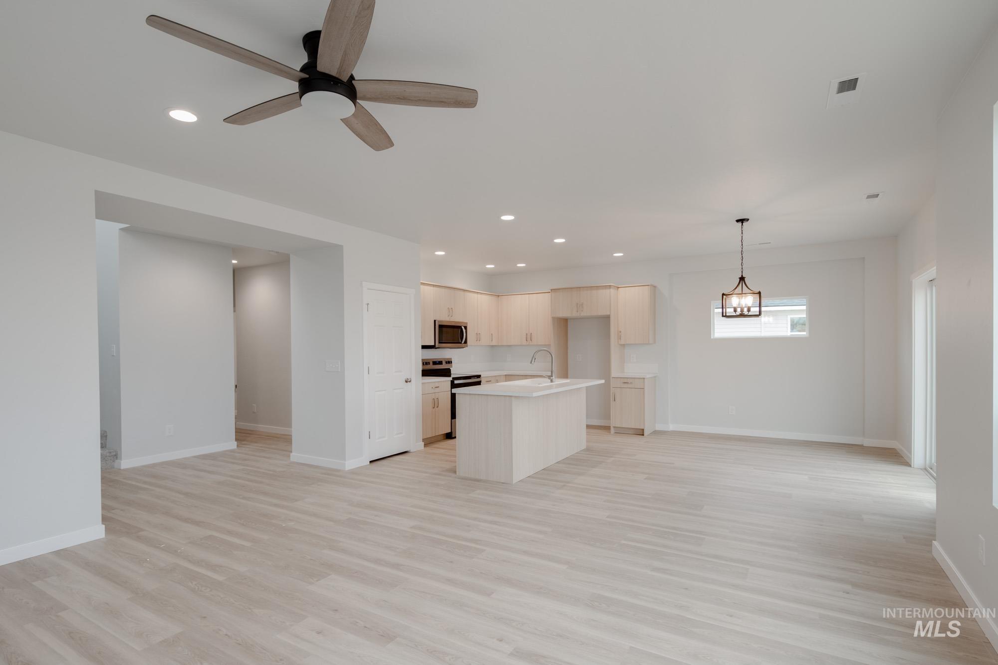 Kitchen featuring open floor plan, a kitchen island with sink, light wood finished floors, light countertops, and appliances with stainless steel finishes