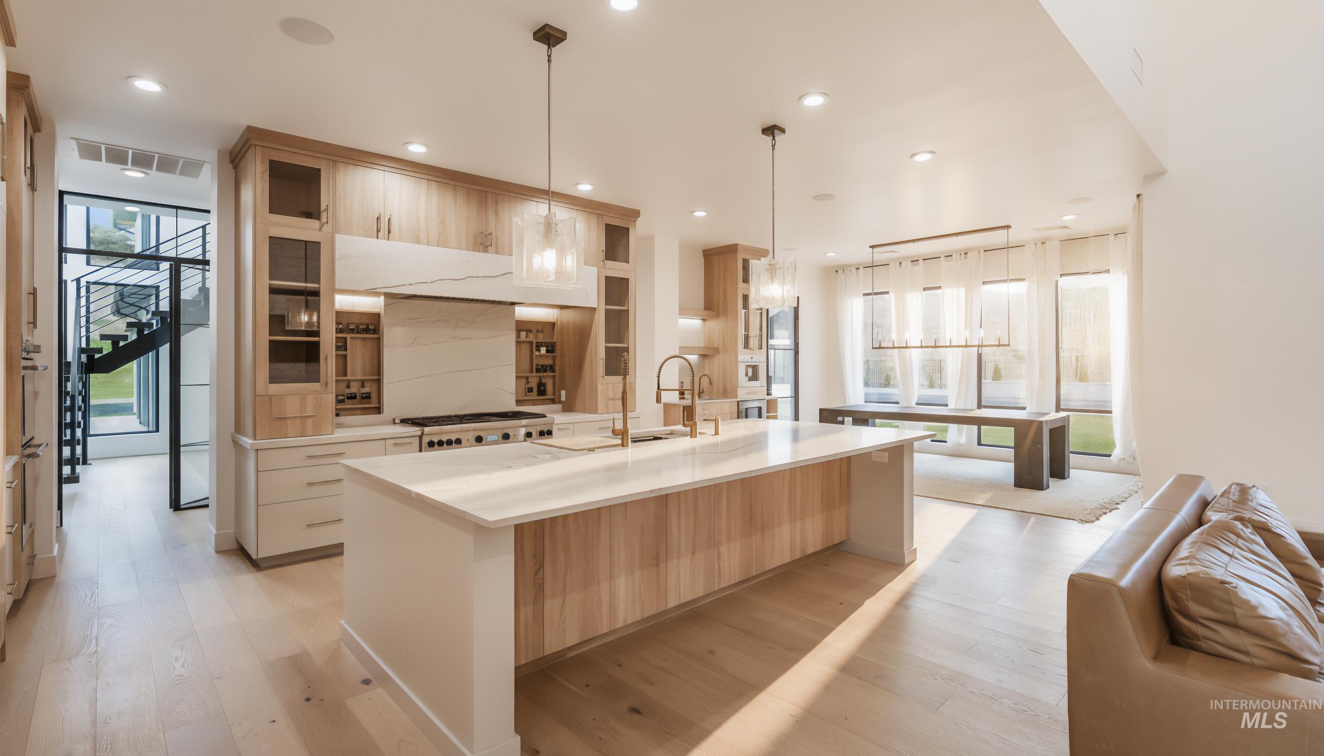 Kitchen with glass insert cabinets, light brown cabinets, hanging light fixtures, light wood-style floors, and a spacious island