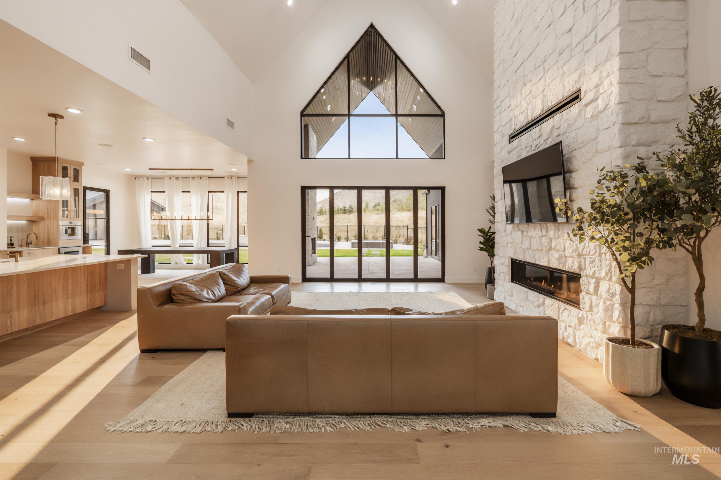 Living room with light wood finished floors, recessed lighting, a stone fireplace, and a towering ceiling