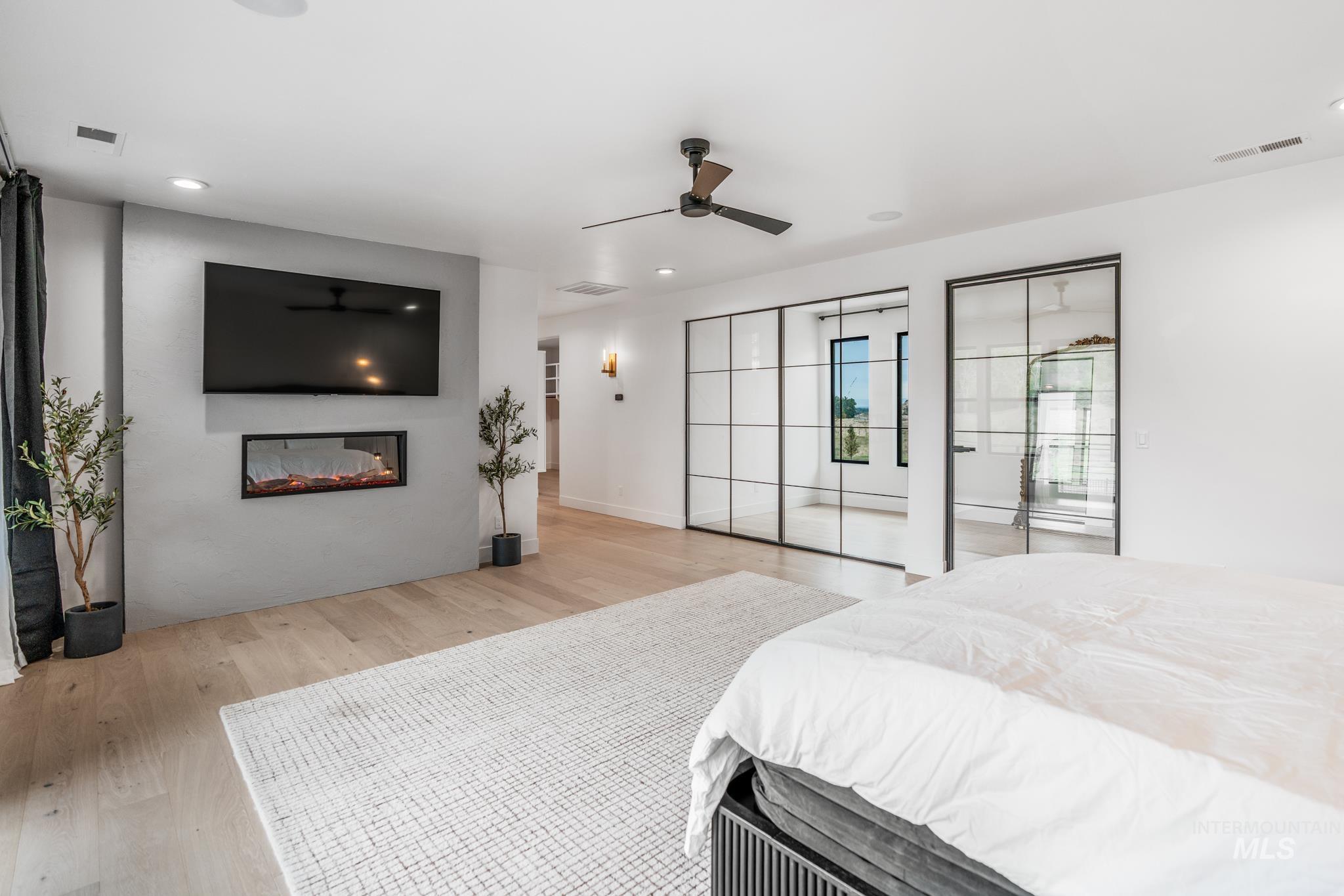 Bedroom featuring light wood-style floors, a glass covered fireplace, a ceiling fan, and recessed lighting