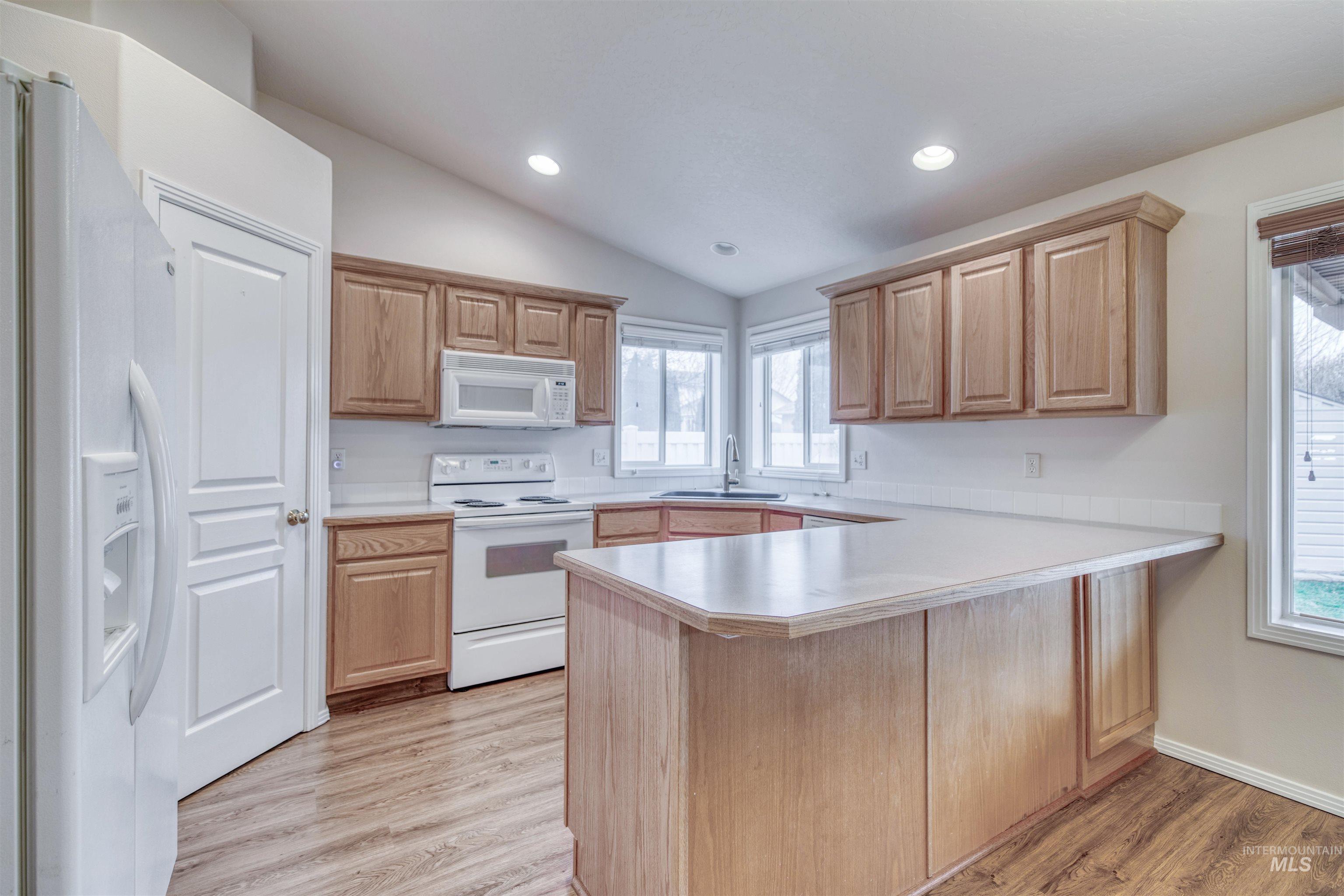 Kitchen featuring light countertops, white appliances, a peninsula, light wood-style floors, and vaulted ceiling