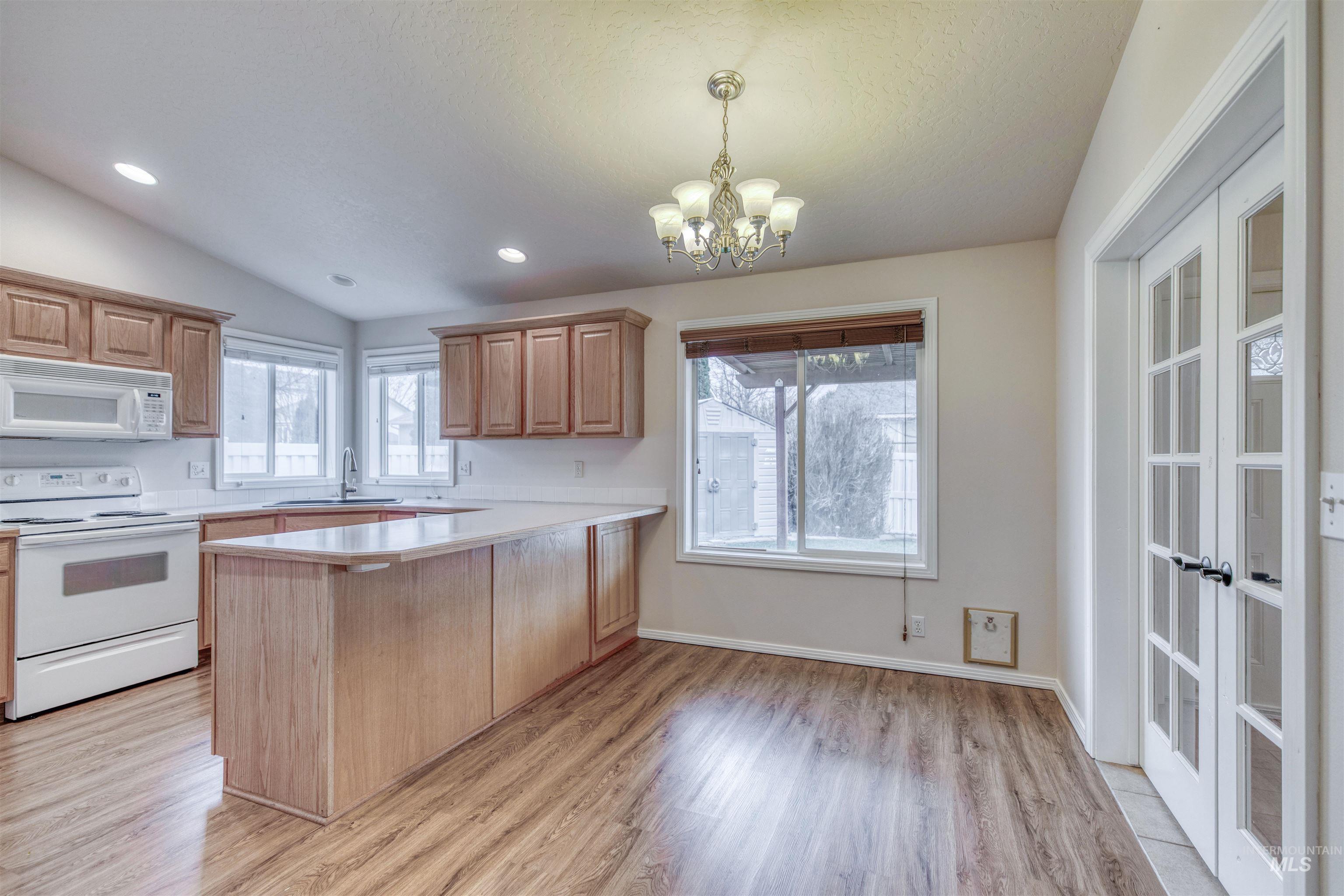 Kitchen featuring white appliances, light countertops, a peninsula, pendant lighting, and light wood-style flooring