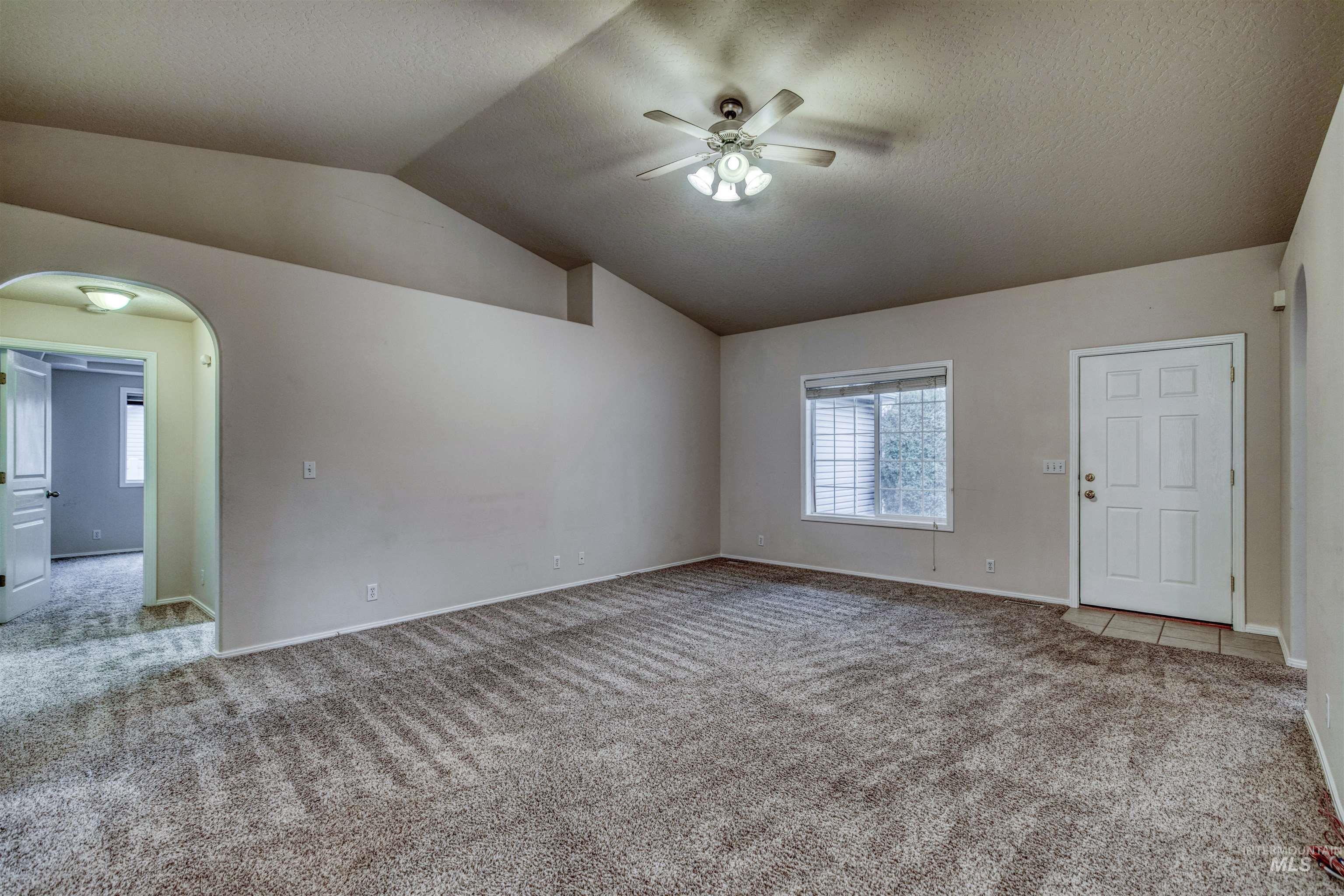 Spare room featuring arched walkways, carpet, vaulted ceiling, a textured ceiling, and a ceiling fan
