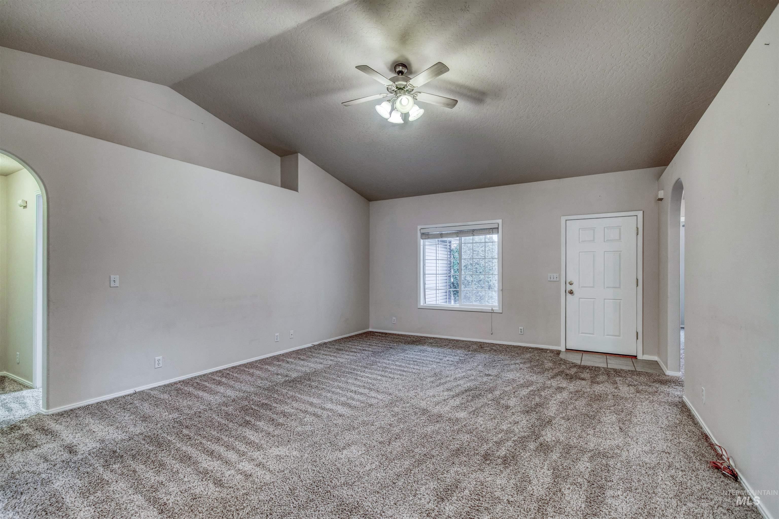 Unfurnished room featuring arched walkways, carpet flooring, a textured ceiling, and vaulted ceiling