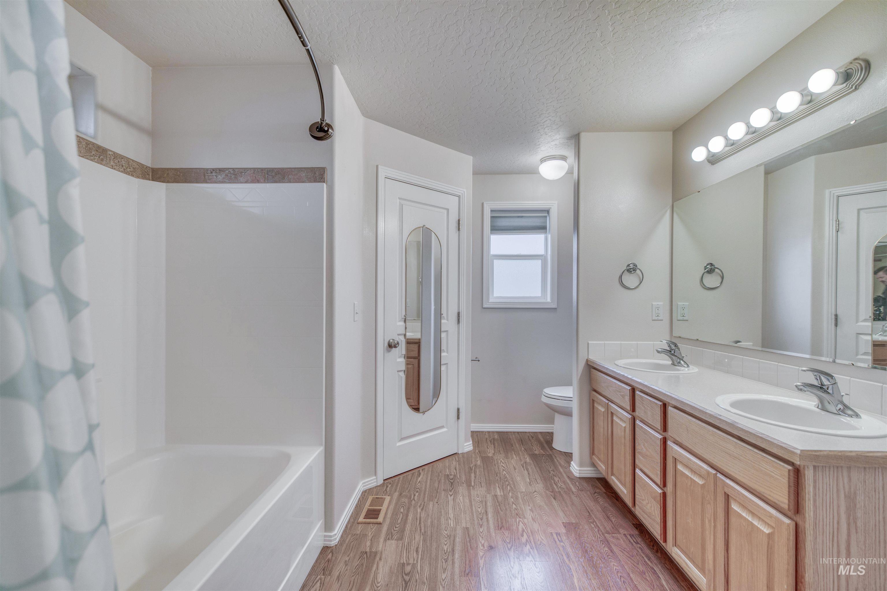 Full bathroom with a textured ceiling, shower / tub combo, double vanity, and light wood-type flooring