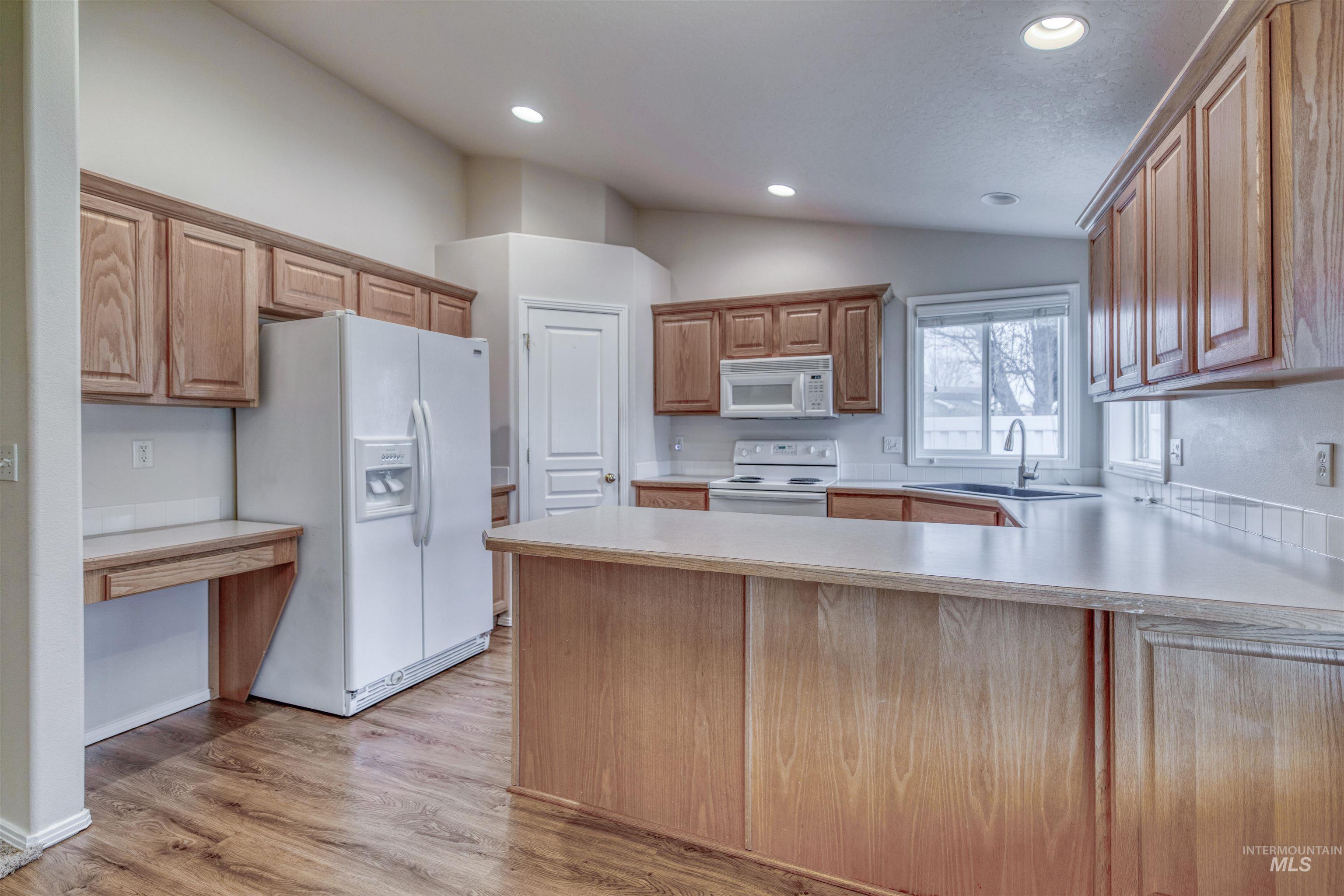 Kitchen featuring a peninsula, light countertops, white appliances, light wood-style floors, and lofted ceiling