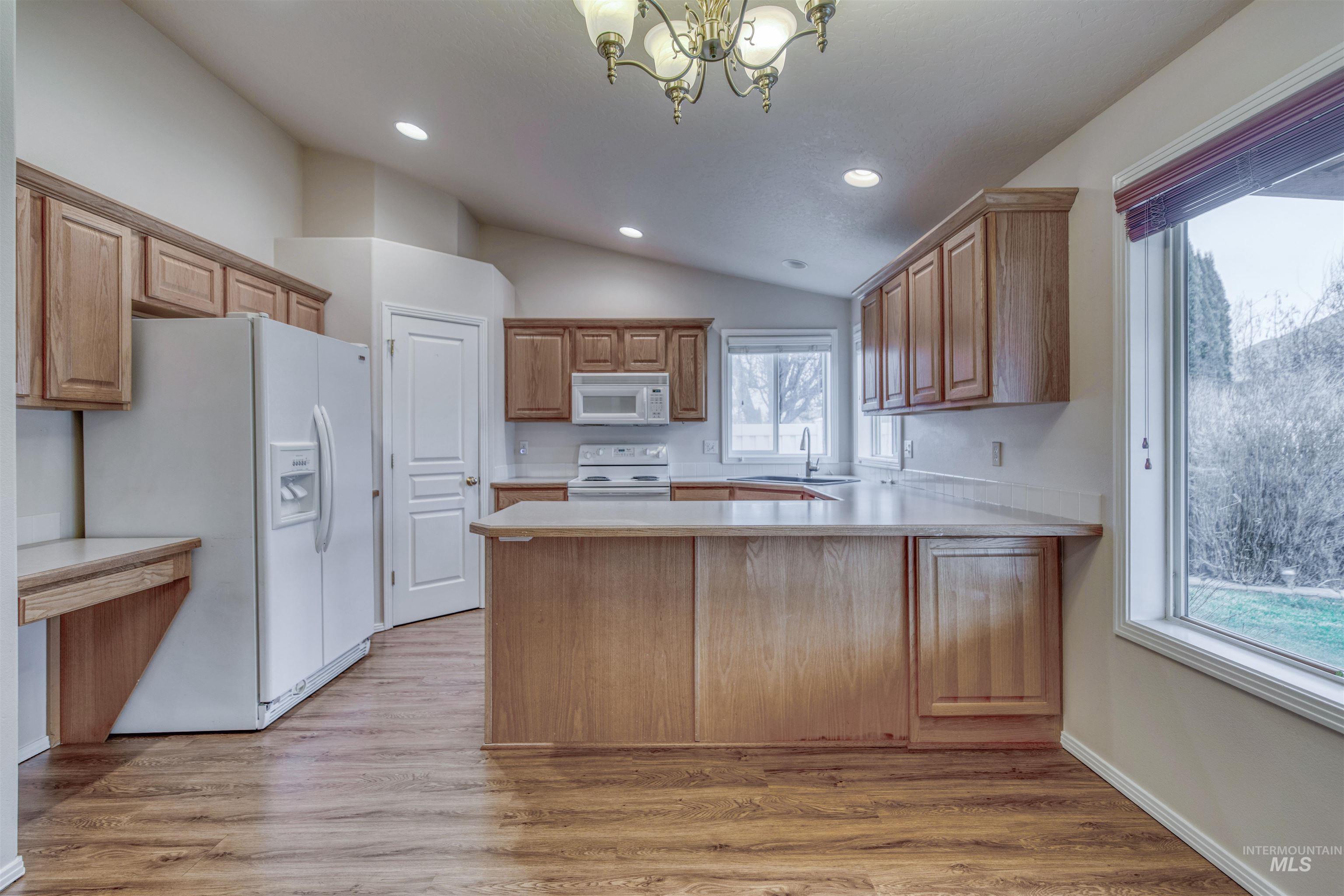 Kitchen with light countertops, a peninsula, white appliances, lofted ceiling, and light wood-style flooring