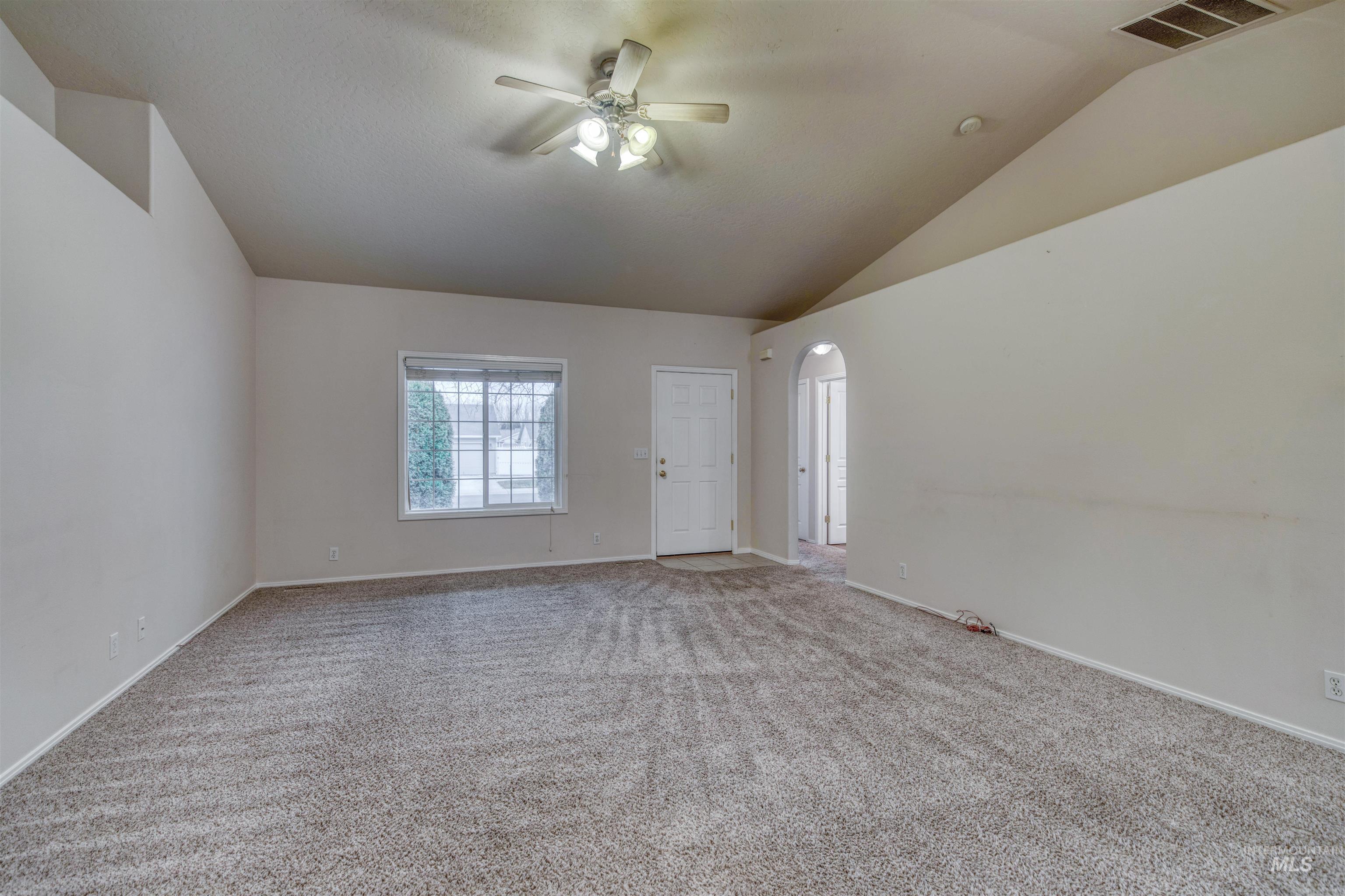 Carpeted empty room featuring arched walkways, a ceiling fan, and lofted ceiling