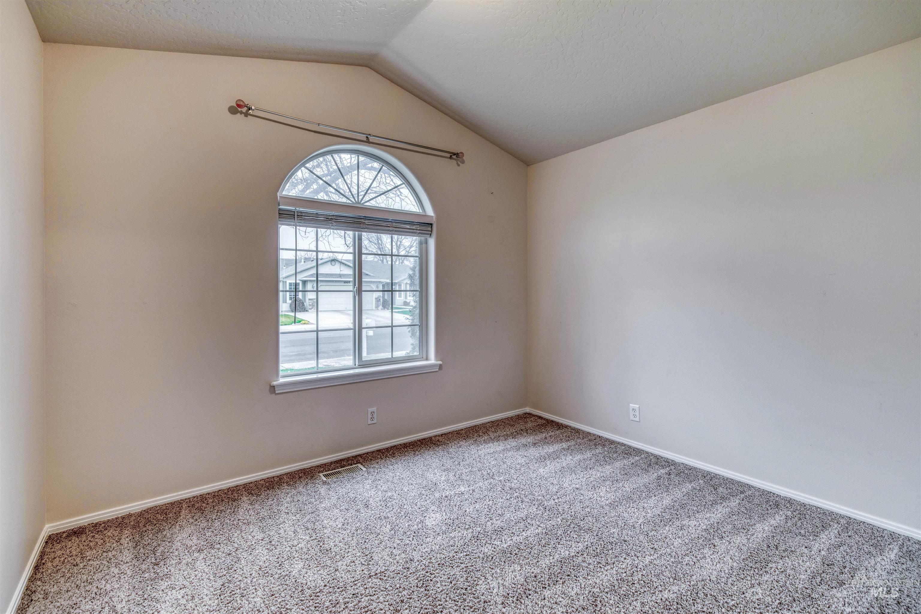 Unfurnished room with lofted ceiling, carpet flooring, and a textured ceiling