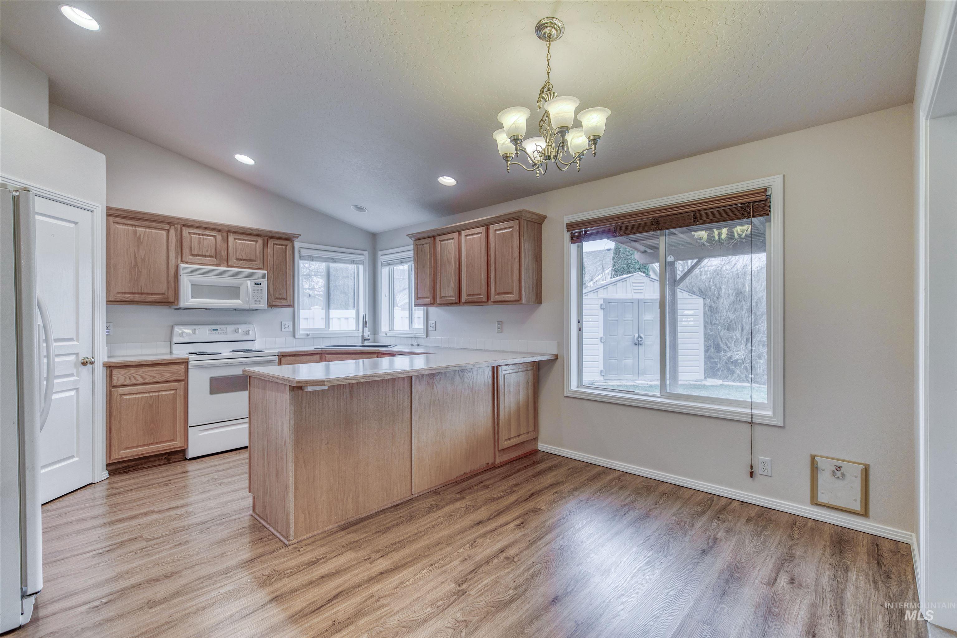 Kitchen with light countertops, white appliances, a peninsula, decorative light fixtures, and vaulted ceiling