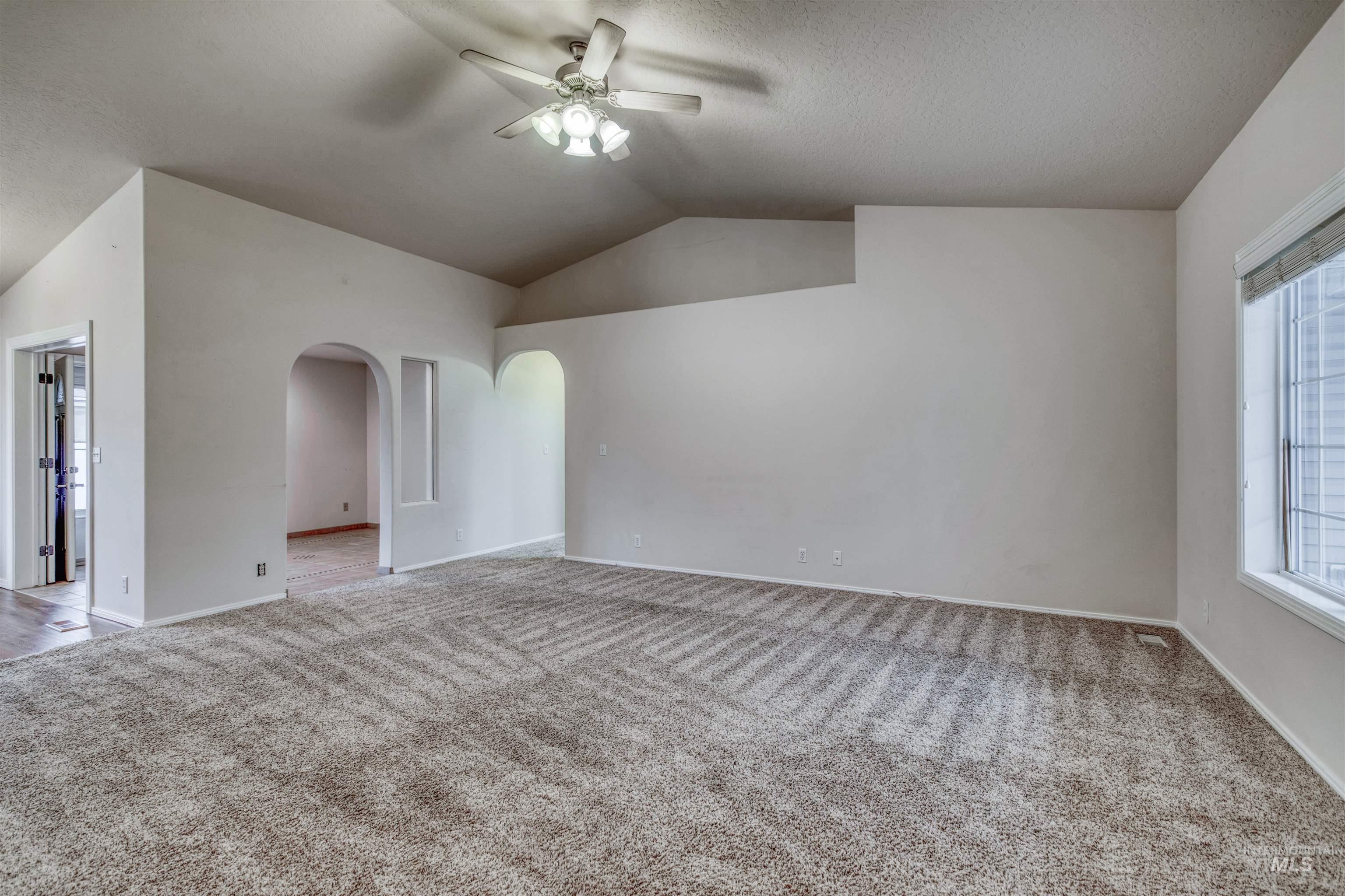 Unfurnished room featuring vaulted ceiling, carpet floors, ceiling fan, and arched walkways