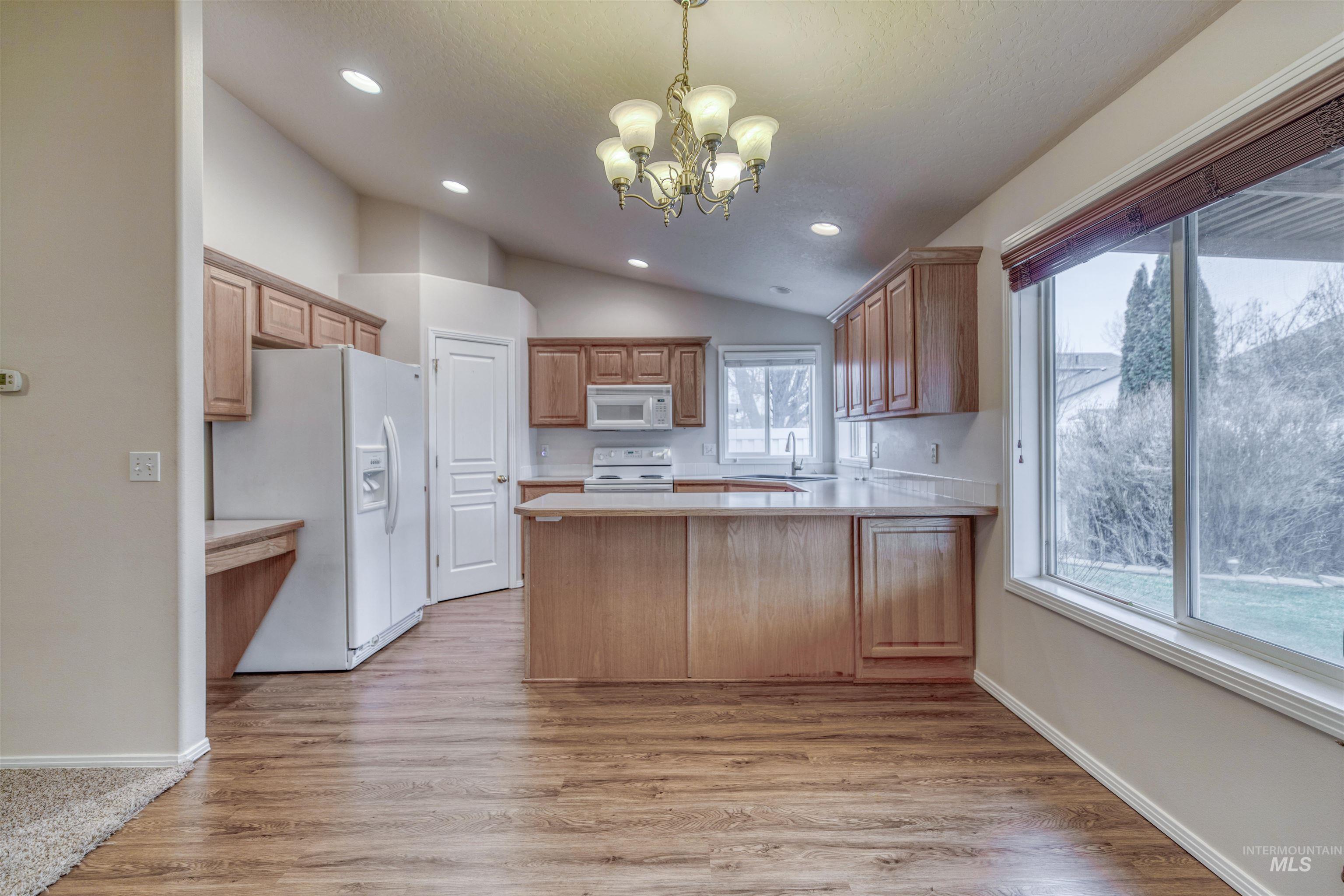 Kitchen featuring a peninsula, hanging light fixtures, white appliances, light countertops, and light wood-type flooring