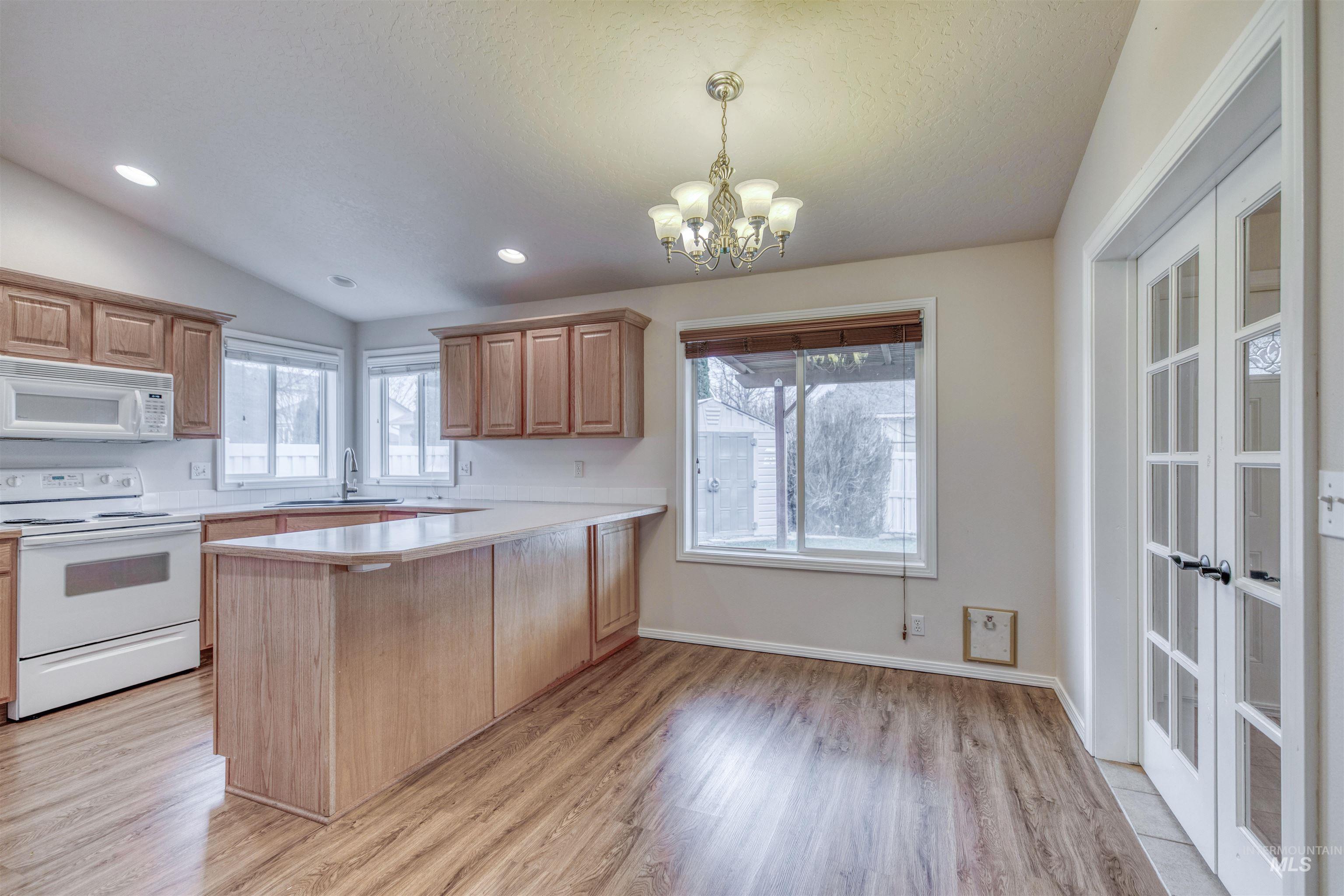Kitchen featuring white appliances, light countertops, a peninsula, pendant lighting, and light wood-type flooring