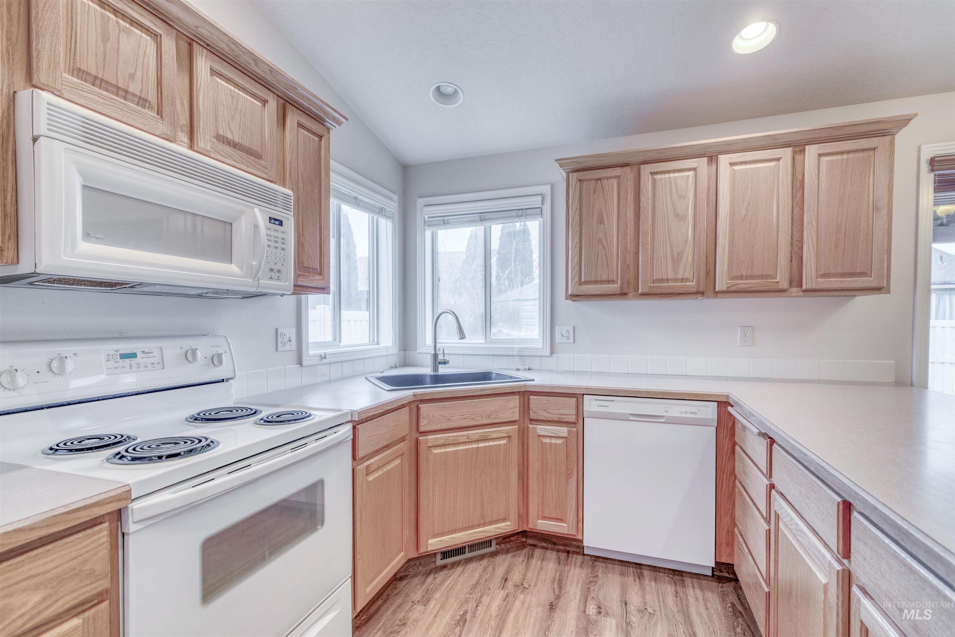Kitchen with white appliances, light countertops, light wood-style flooring, light brown cabinets, and vaulted ceiling