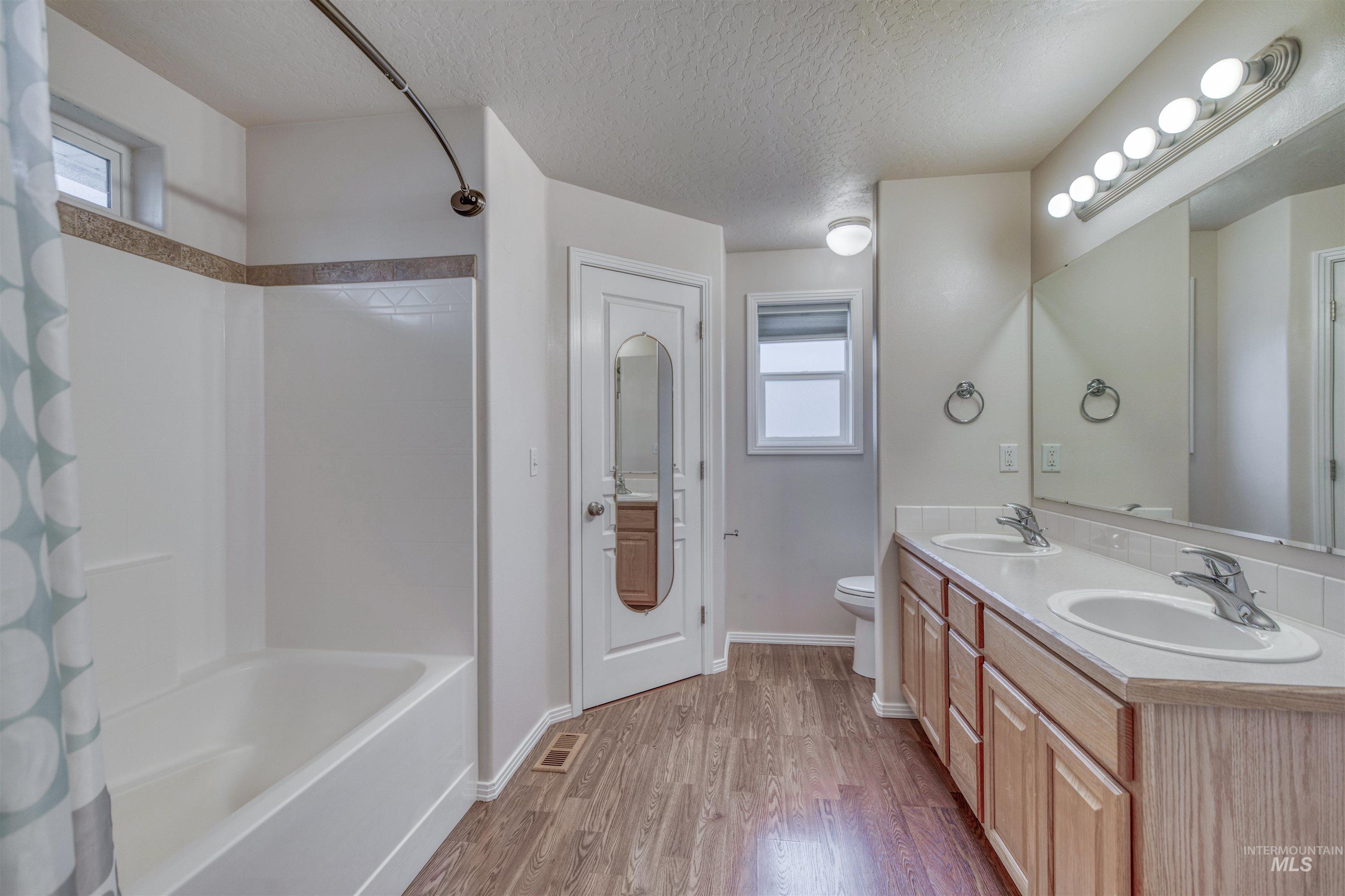 Full bath featuring a textured ceiling, shower / tub combo with curtain, double vanity, and light wood finished floors