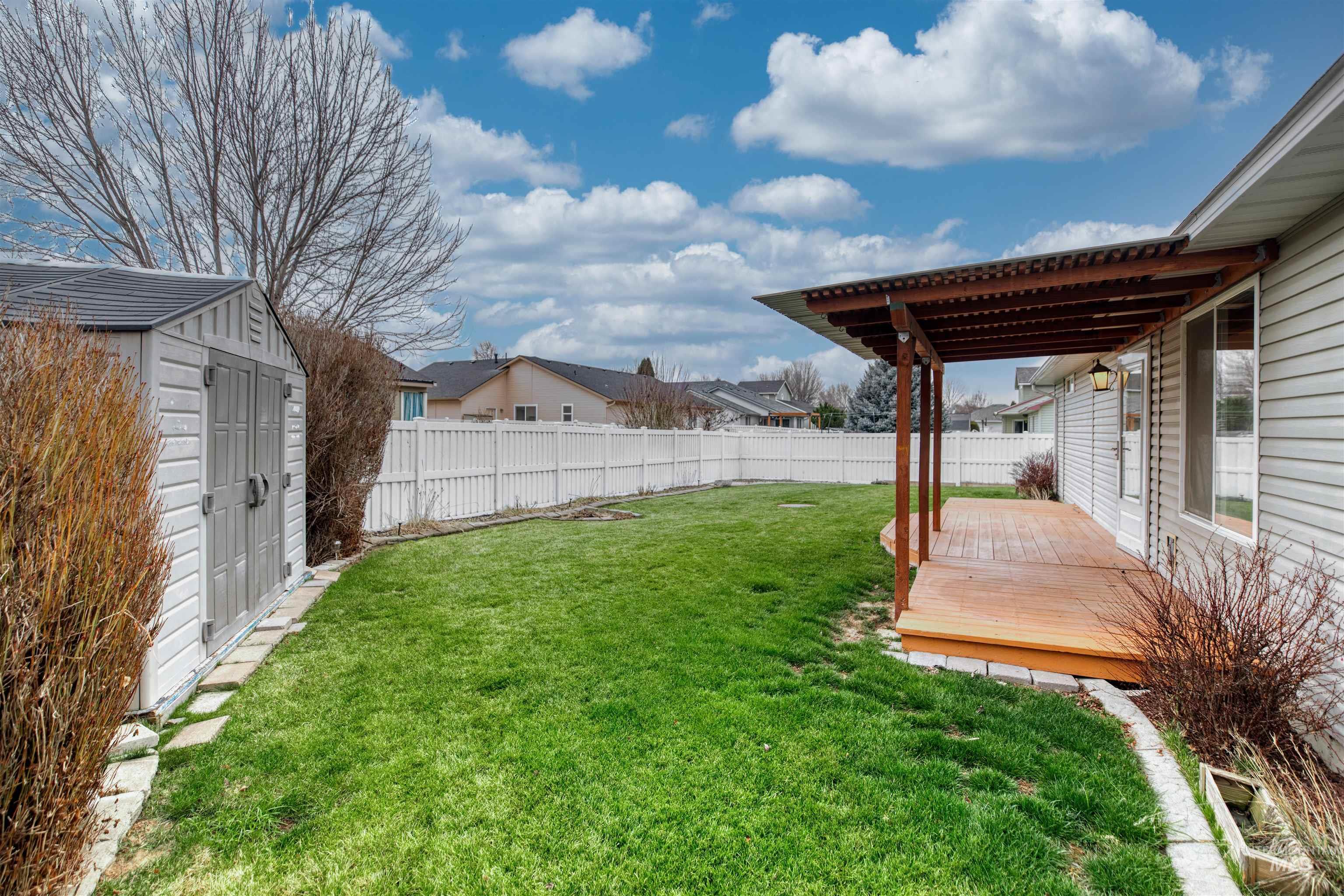Fenced backyard featuring a wooden deck, a storage shed, and a residential view