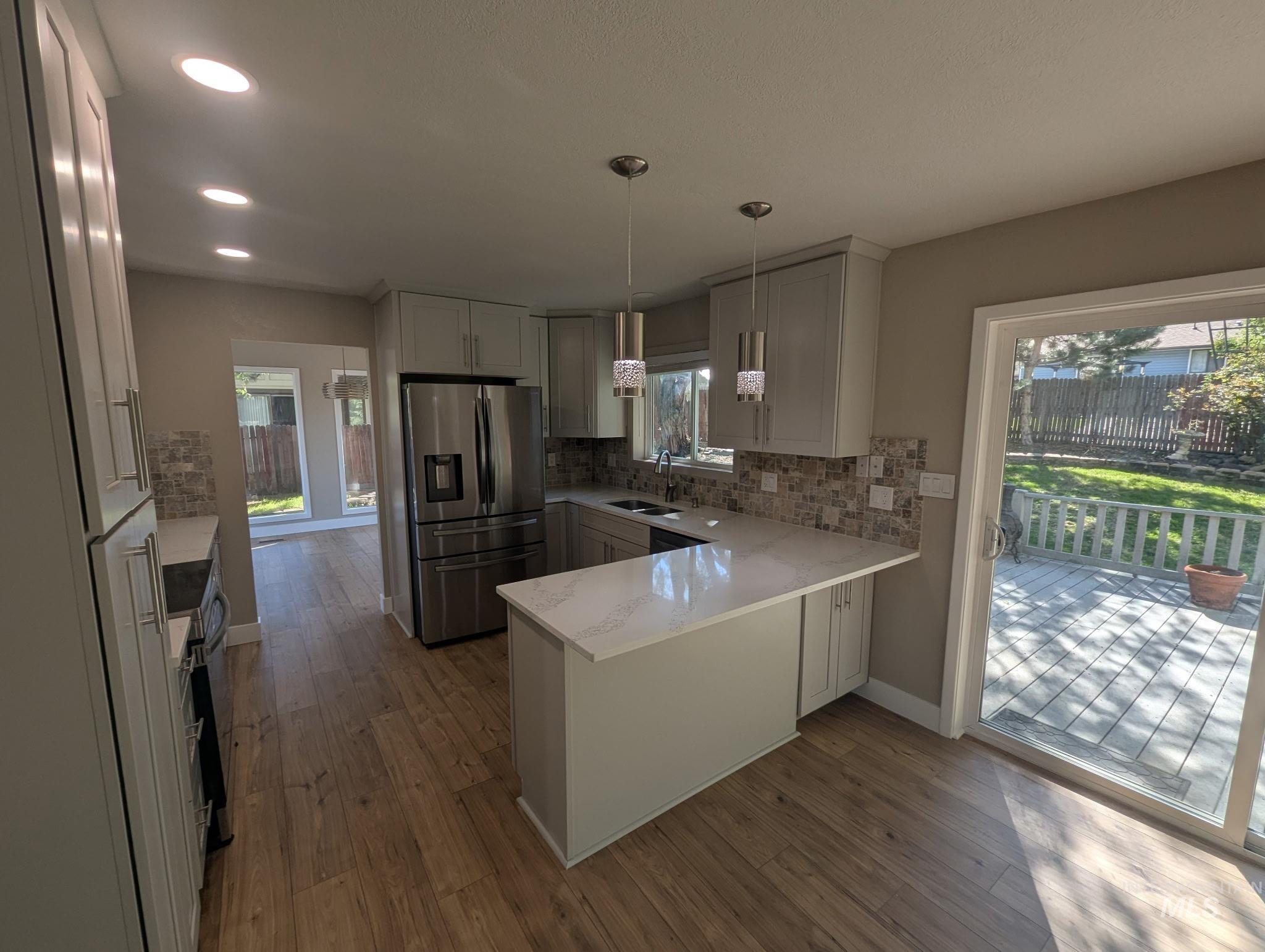 Kitchen with a peninsula, stainless steel appliances, light stone counters, backsplash, and decorative light fixtures