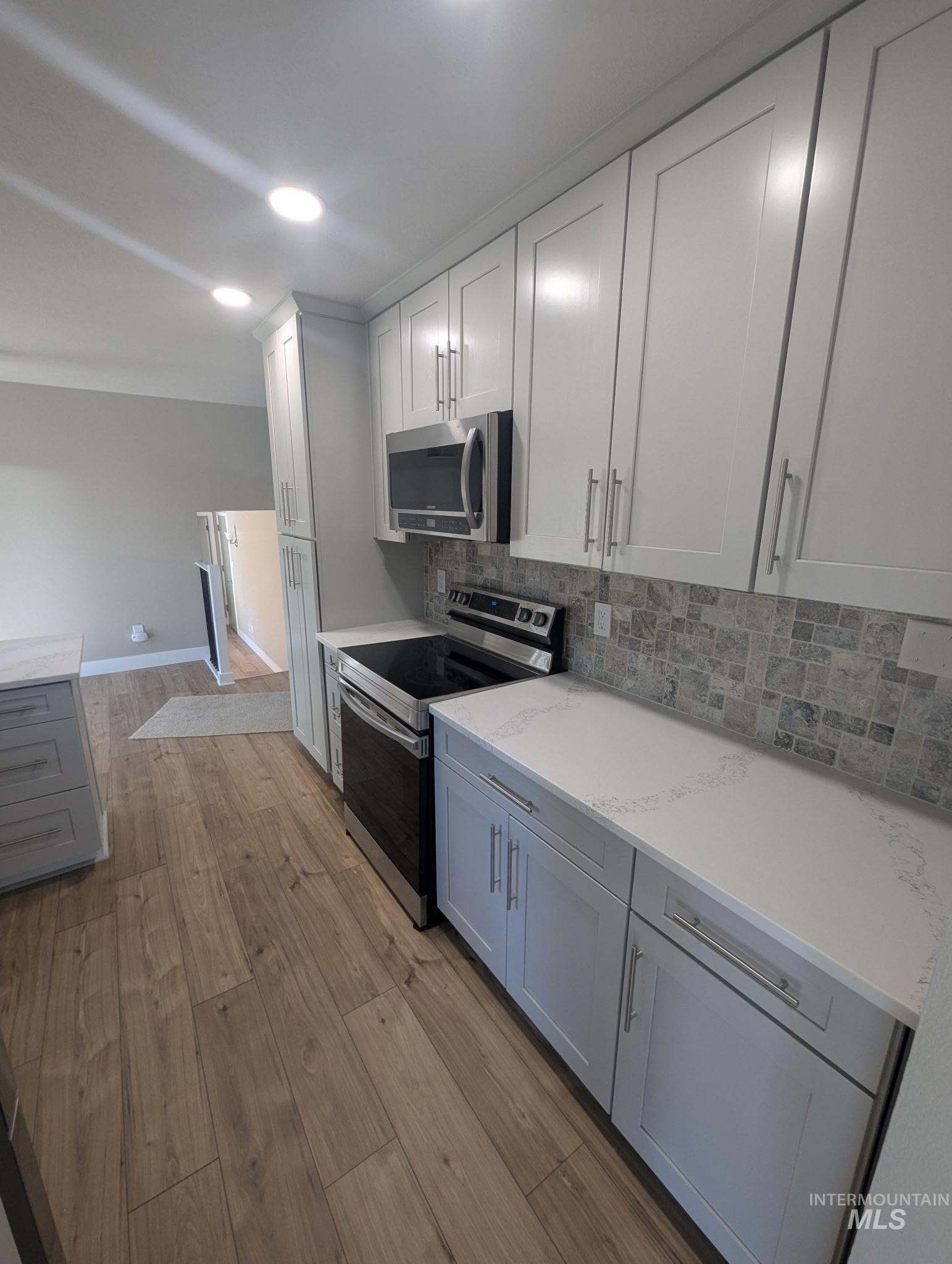 Kitchen featuring stainless steel appliances, decorative backsplash, light wood finished floors, light stone counters, and white cabinetry