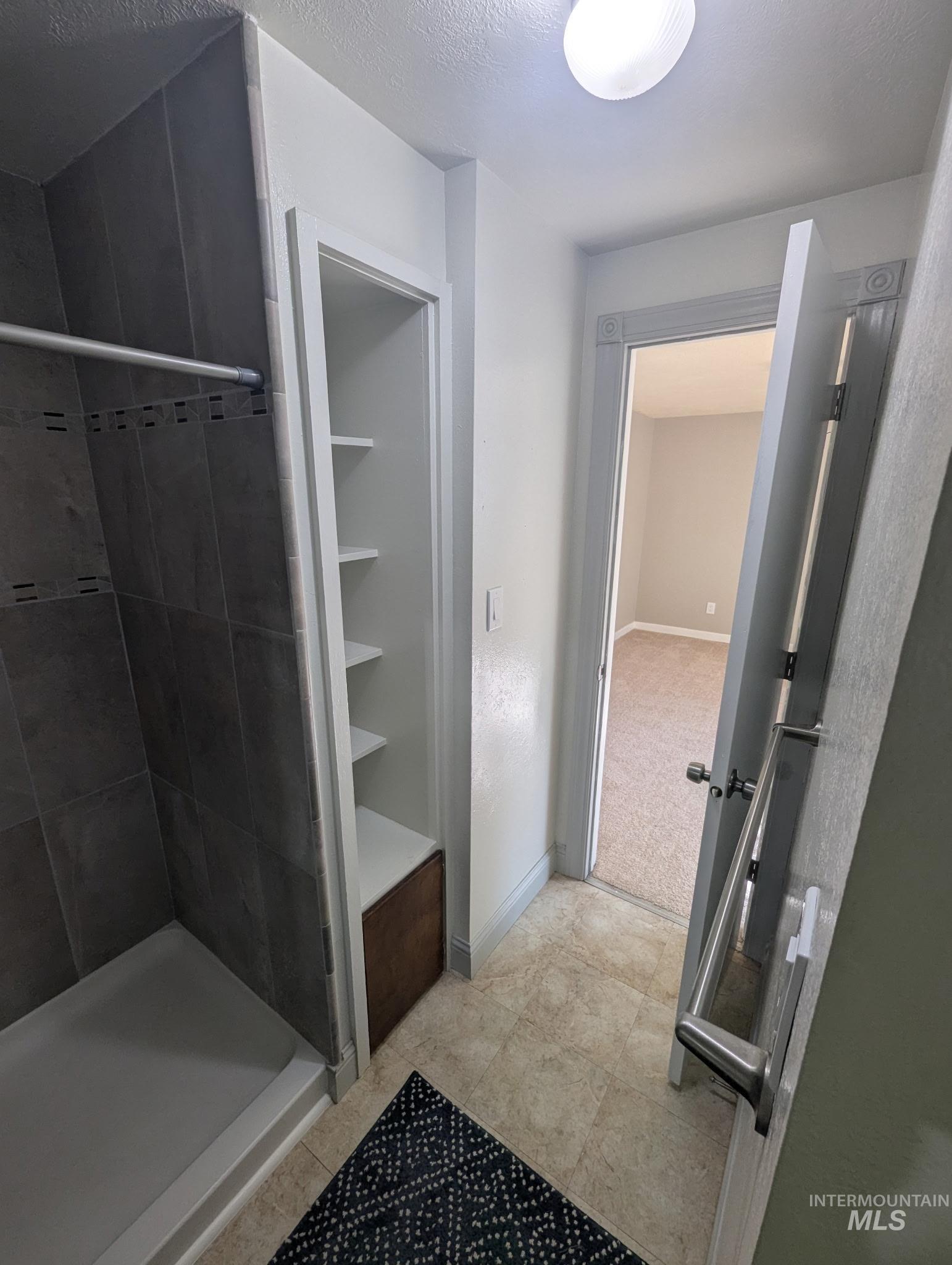 Full bathroom with a shower stall, a textured ceiling, and light tile patterned floors