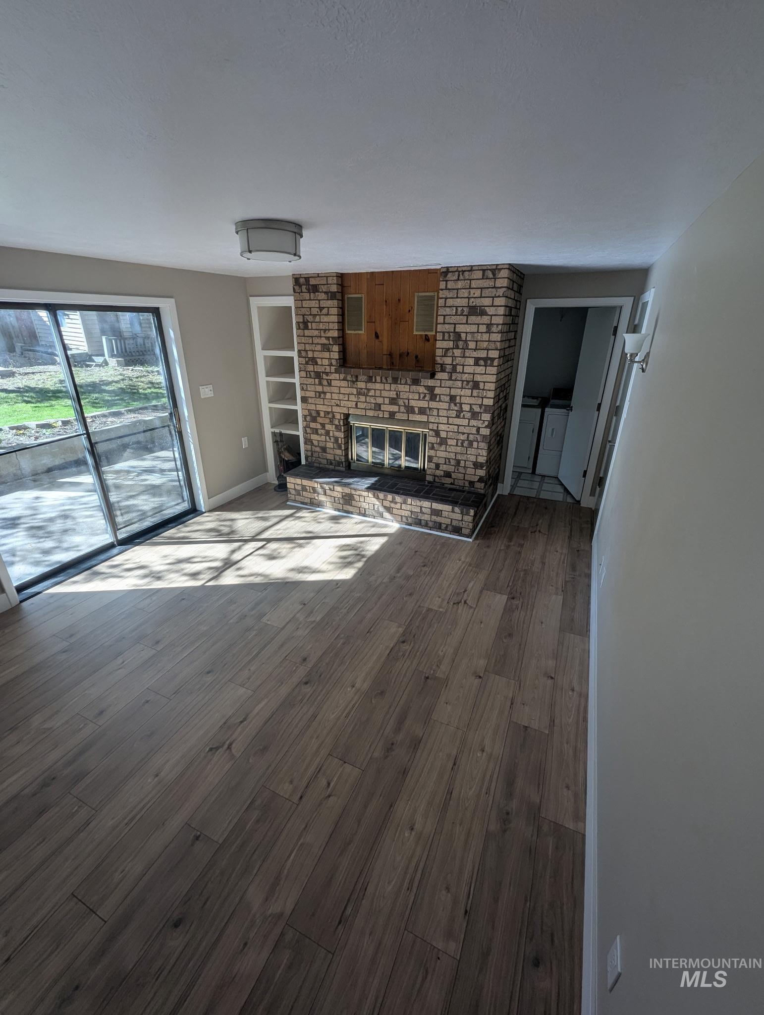 Unfurnished living room with a fireplace, built in shelves, dark wood-type flooring, and washer and dryer