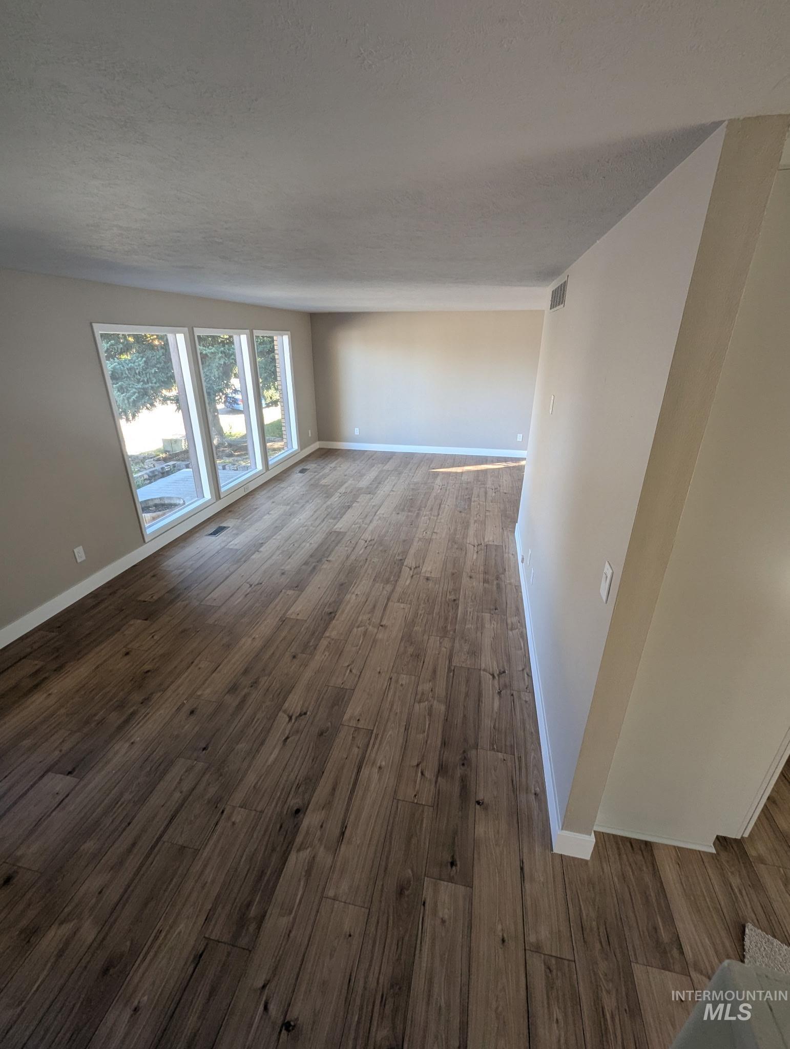 Unfurnished living room featuring dark wood-style flooring and a textured ceiling