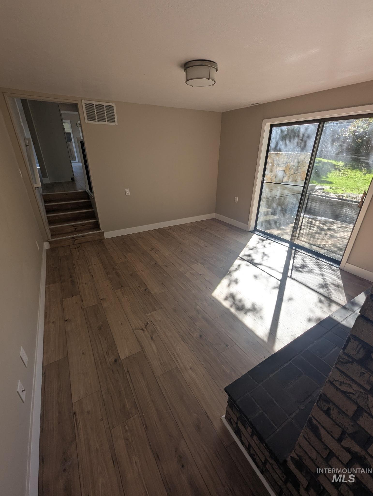 Unfurnished living room with dark wood-style flooring and stairway