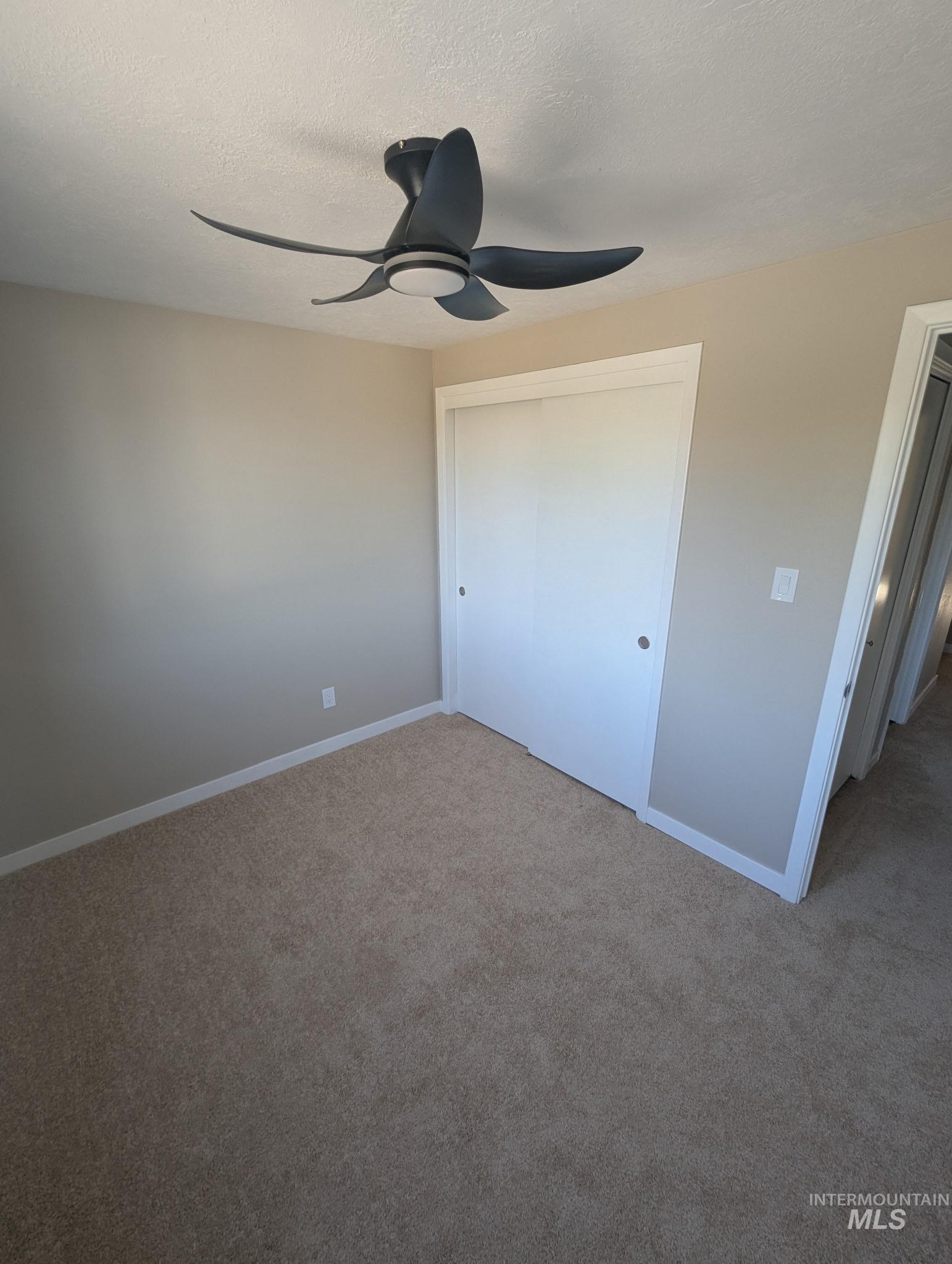 Unfurnished bedroom featuring a textured ceiling, carpet flooring, a closet, and a ceiling fan
