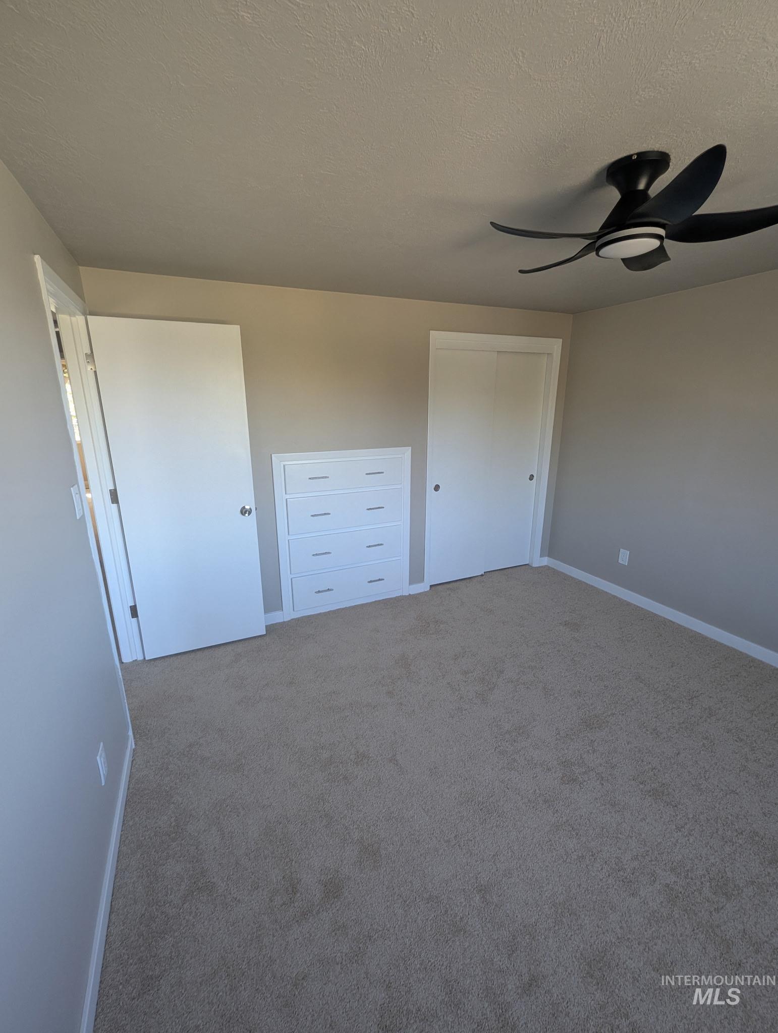 Unfurnished bedroom featuring a textured ceiling, carpet flooring, and a ceiling fan