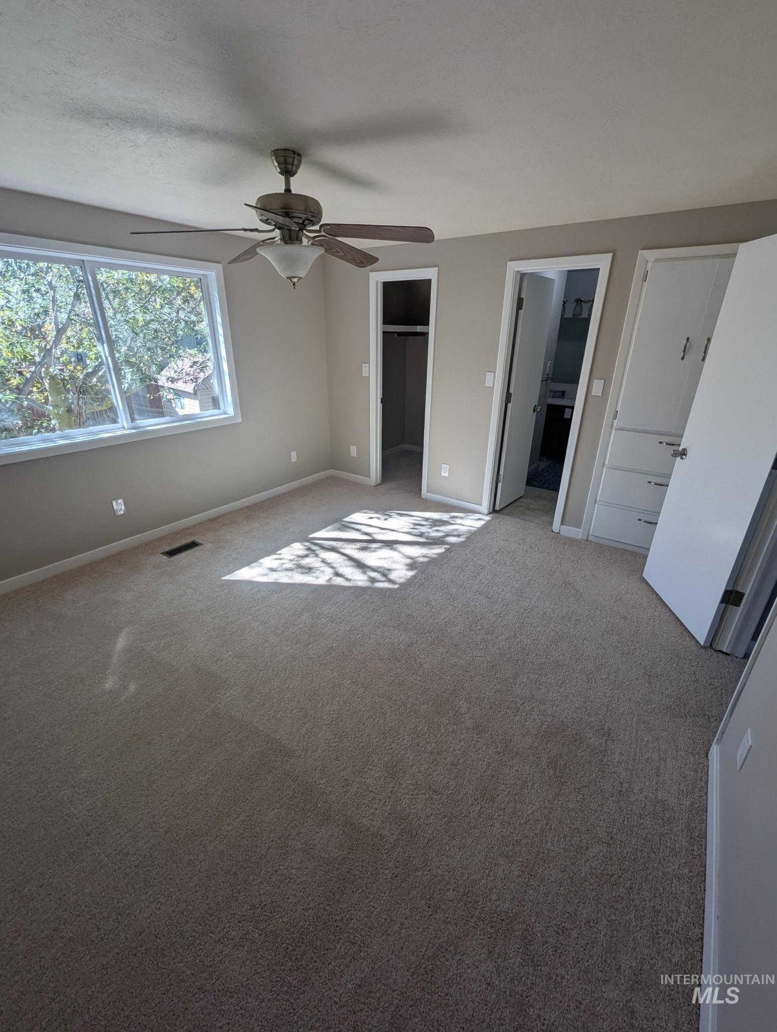 Unfurnished bedroom featuring a walk in closet, carpet floors, and ceiling fan