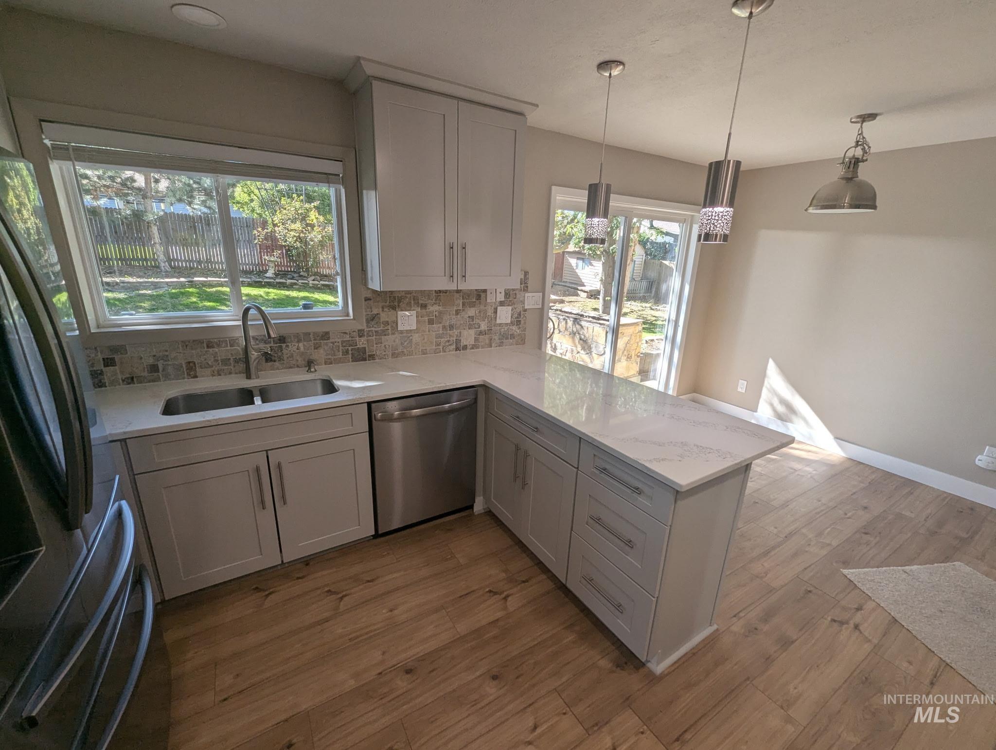 Kitchen with decorative backsplash, stainless steel appliances, hanging light fixtures, light stone counters, and a peninsula