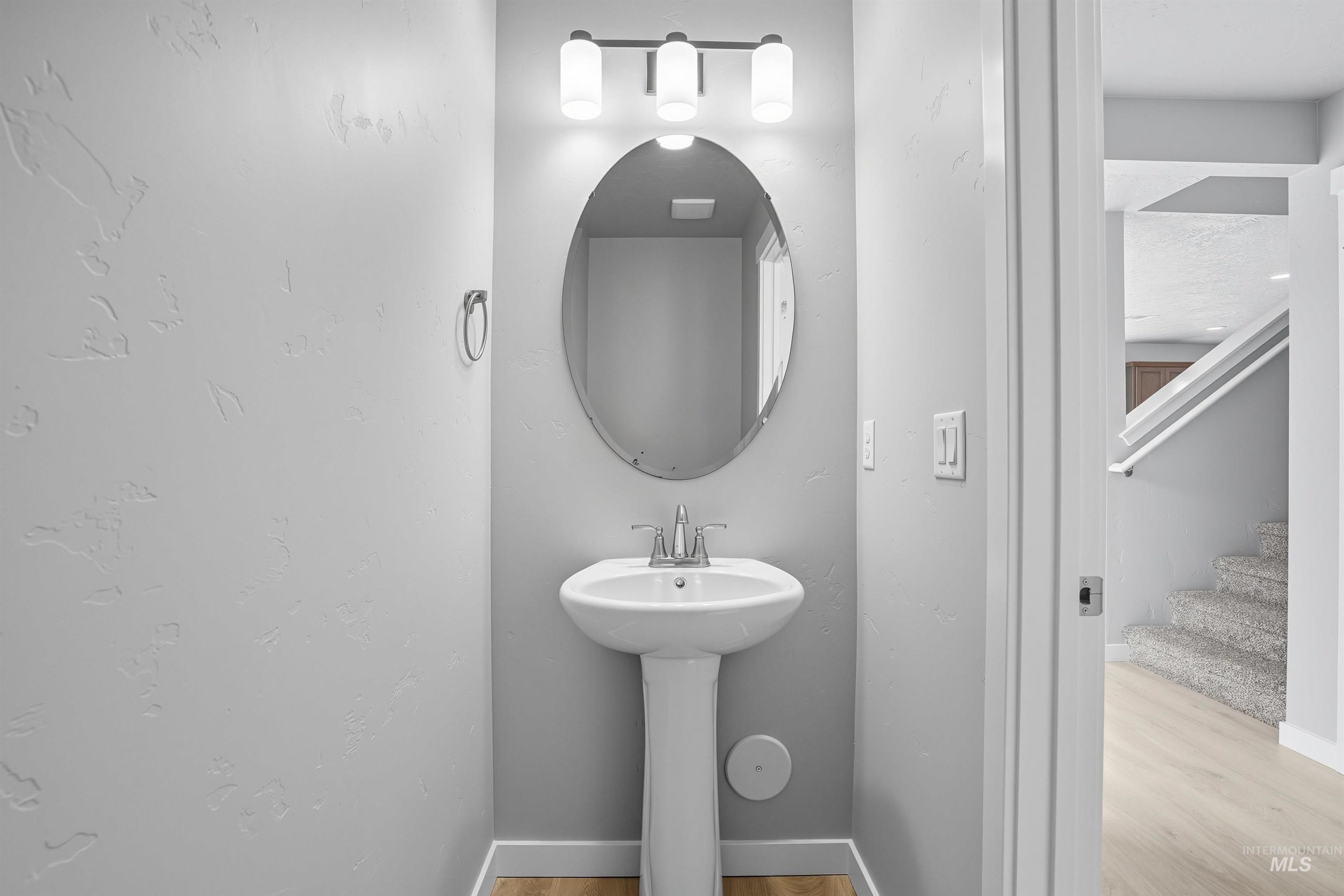 Pedestal sink and oval mirror with a three-bulb vanity light fixture