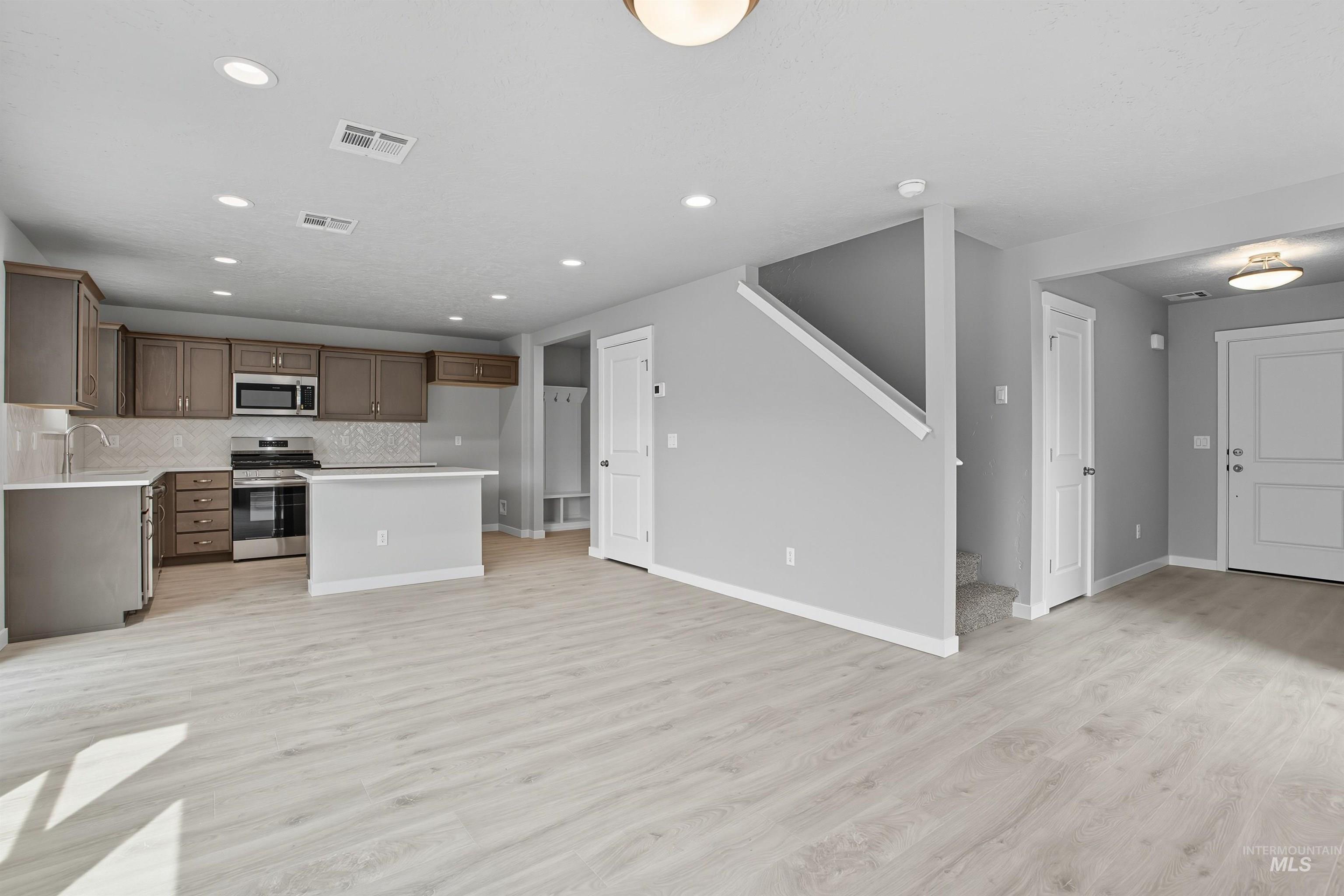 Open-concept kitchen and living area featuring wood-finish flooring, recessed lighting, stainless steel appliances, and a central island with a breakfast bar