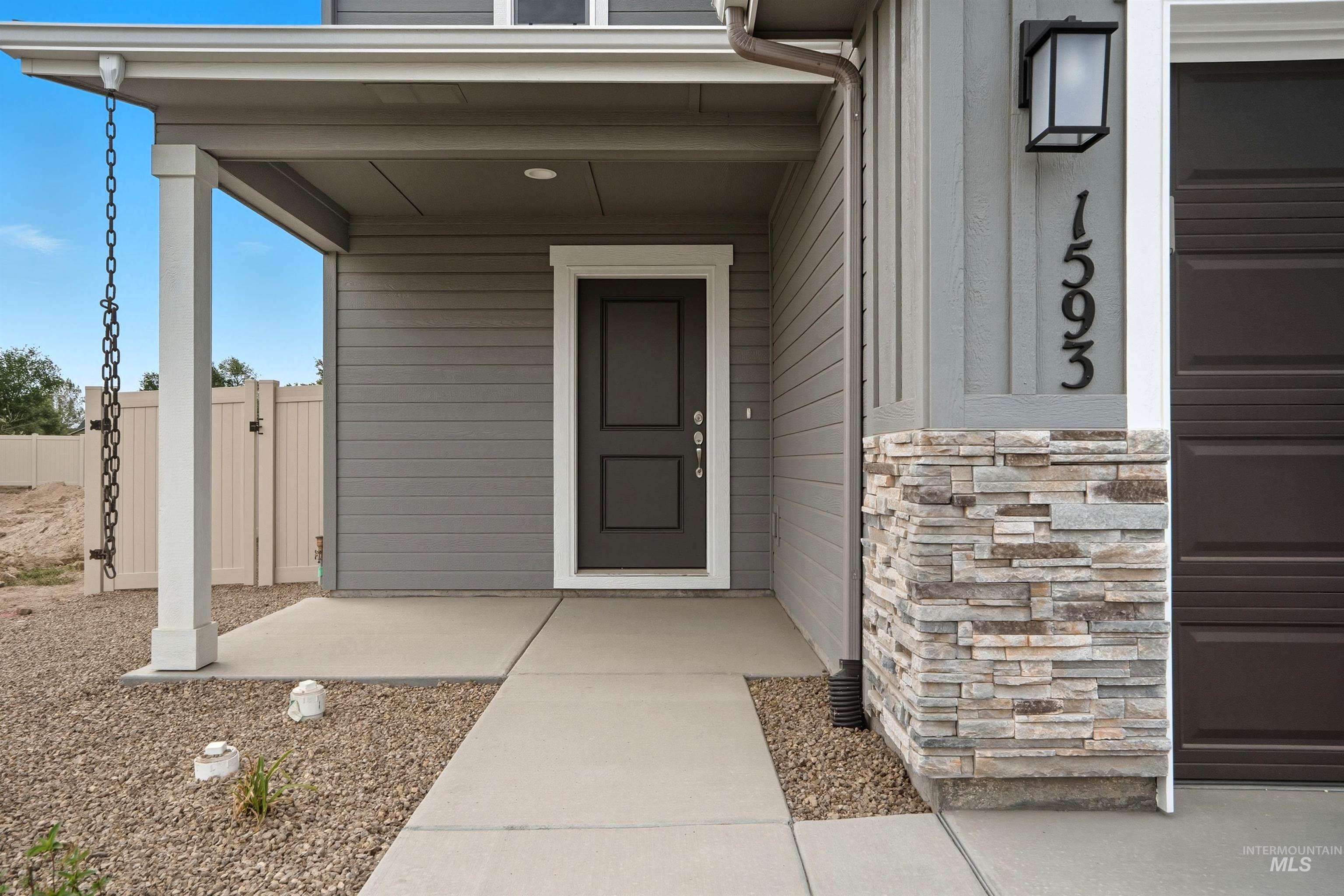 Covered porch entry featuring a dark gray door with white trim, horizontal gray siding, and stacked stone accents