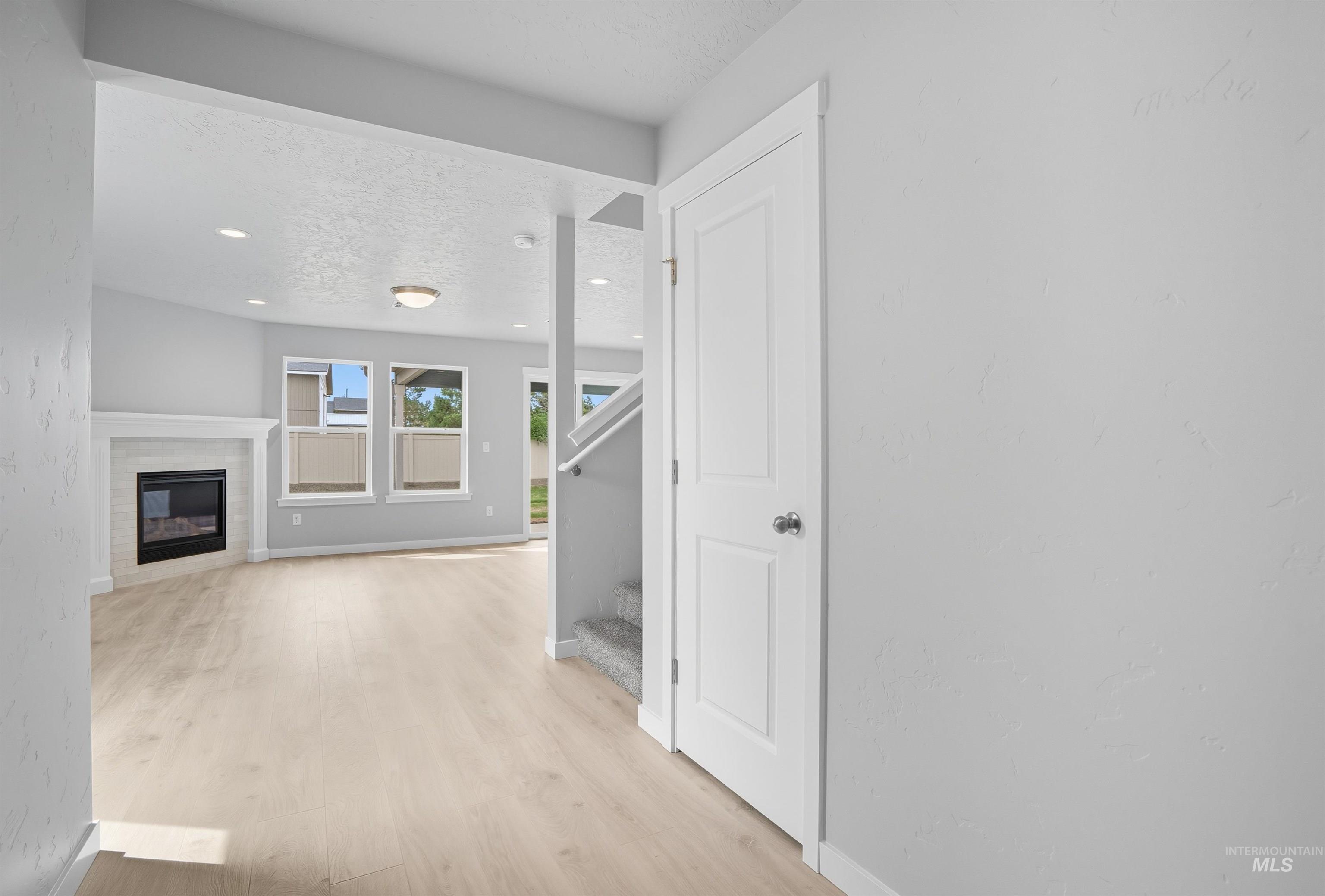 Living area featuring wood-finish flooring, a white mantel fireplace, multiple windows with blinds, recessed lighting, and a neutral color palette